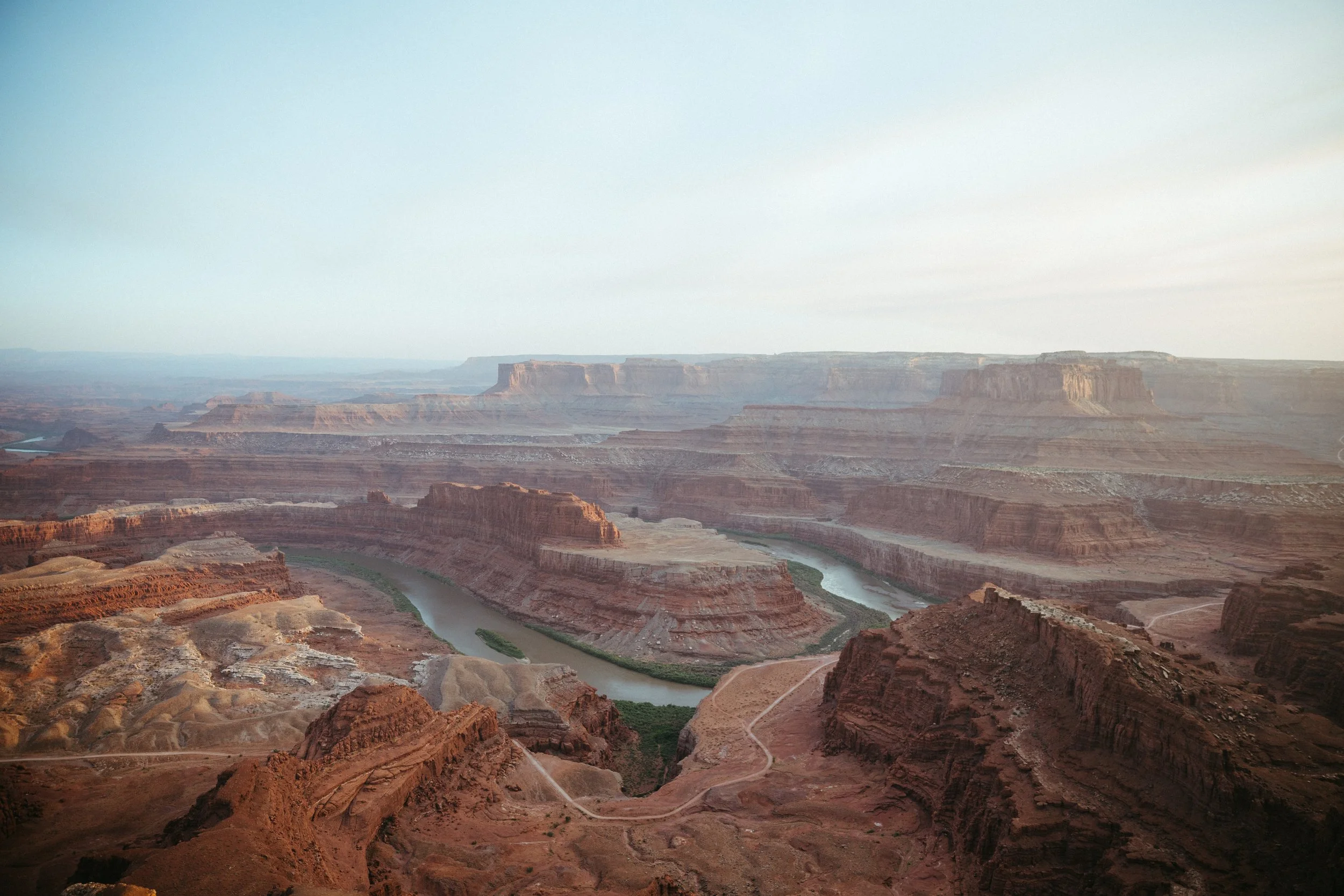 View of the Grand Canyon with a winding river through the canyon, layered rock formations, and a hazy sky.