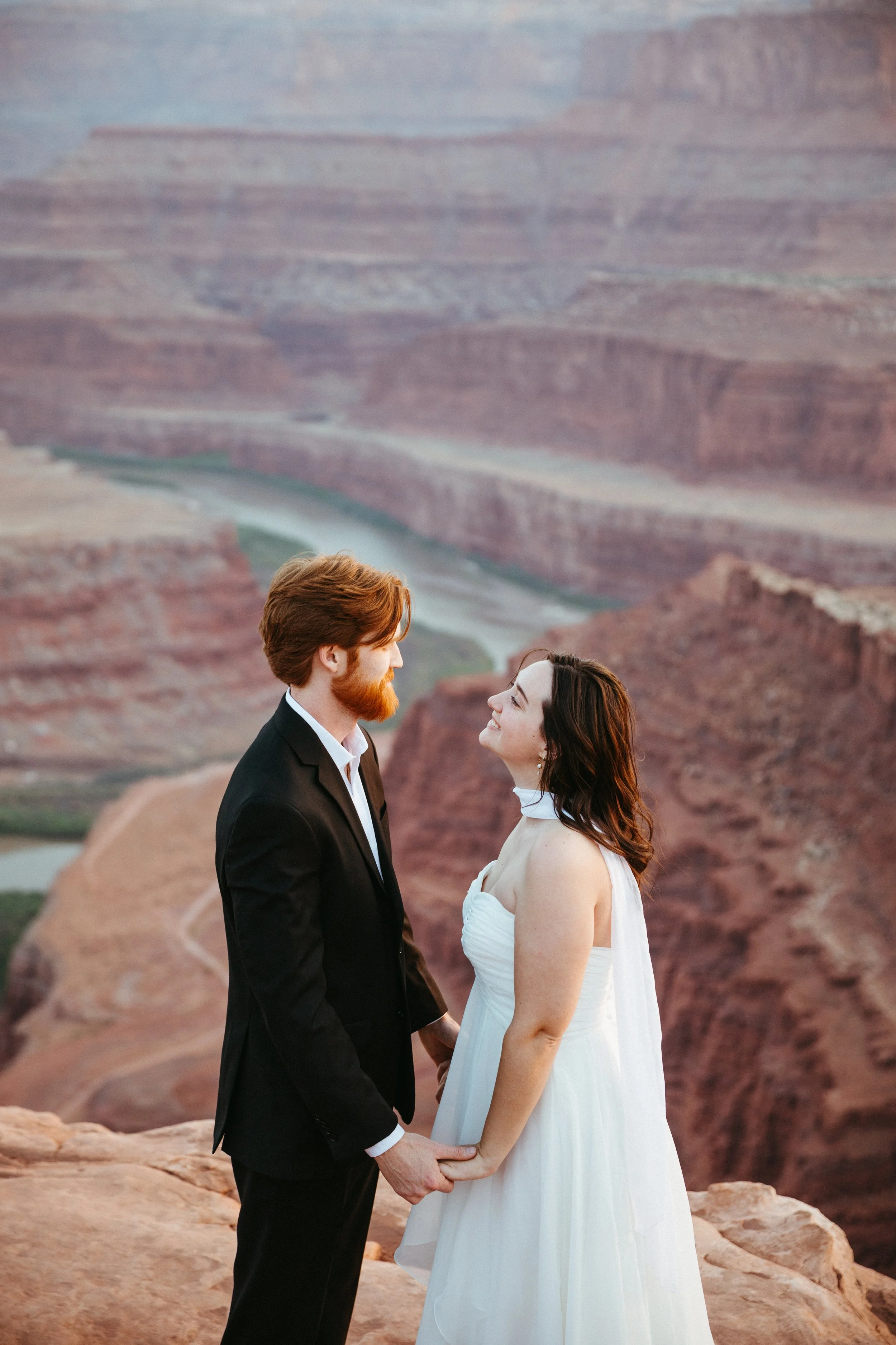 A couple dressed in wedding attire standing and holding hands at the Grand Canyon during sunset.