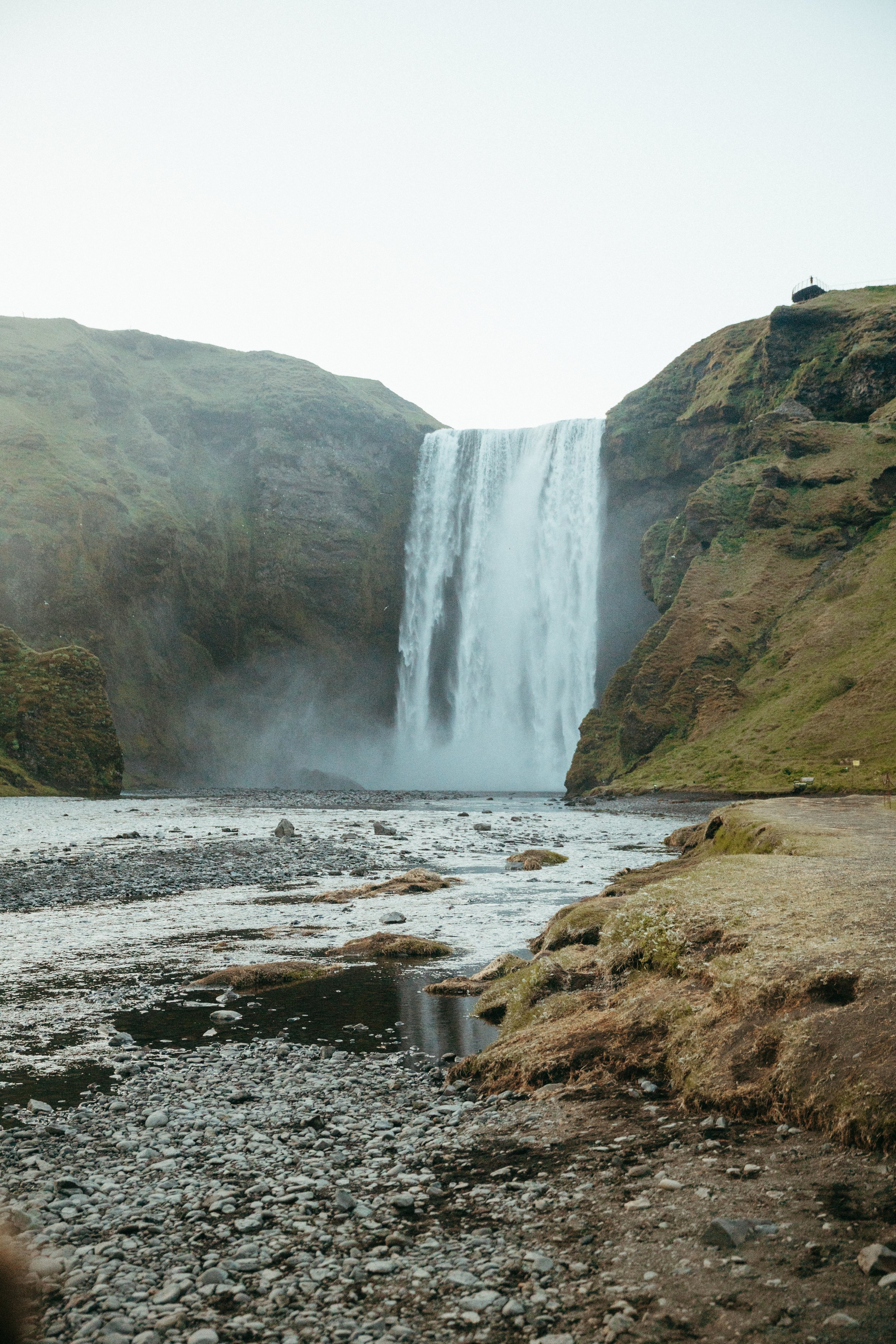 A waterfall flowing into a river surrounded by green hills and rocky terrain