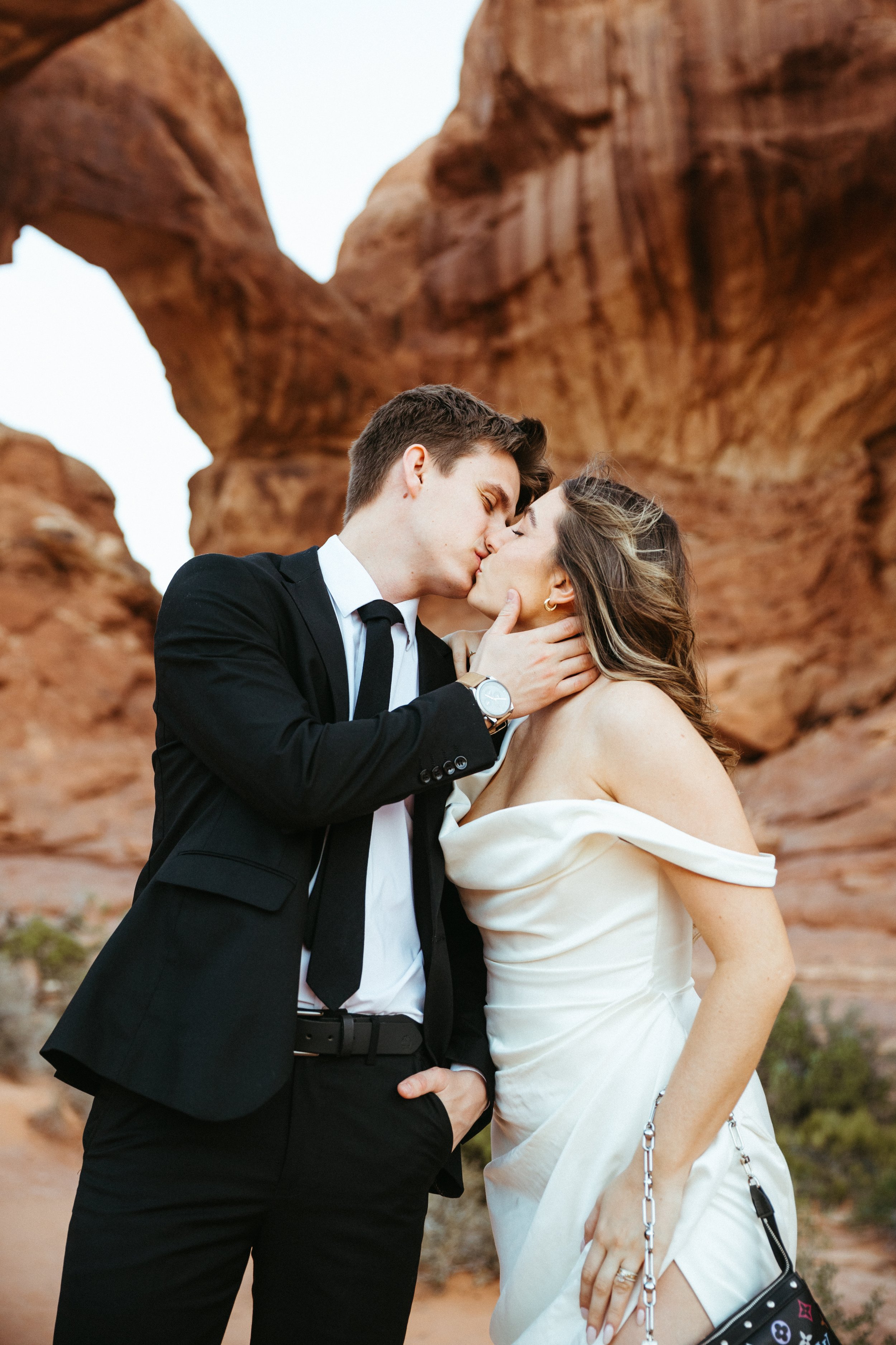 A couple in wedding attire sharing a kiss in front of red rock formations. Moab Utah wedding photographer, Arches National Park elopement photographer, Canyonlands wedding photographer, Capitol Reef elopement photographer.
