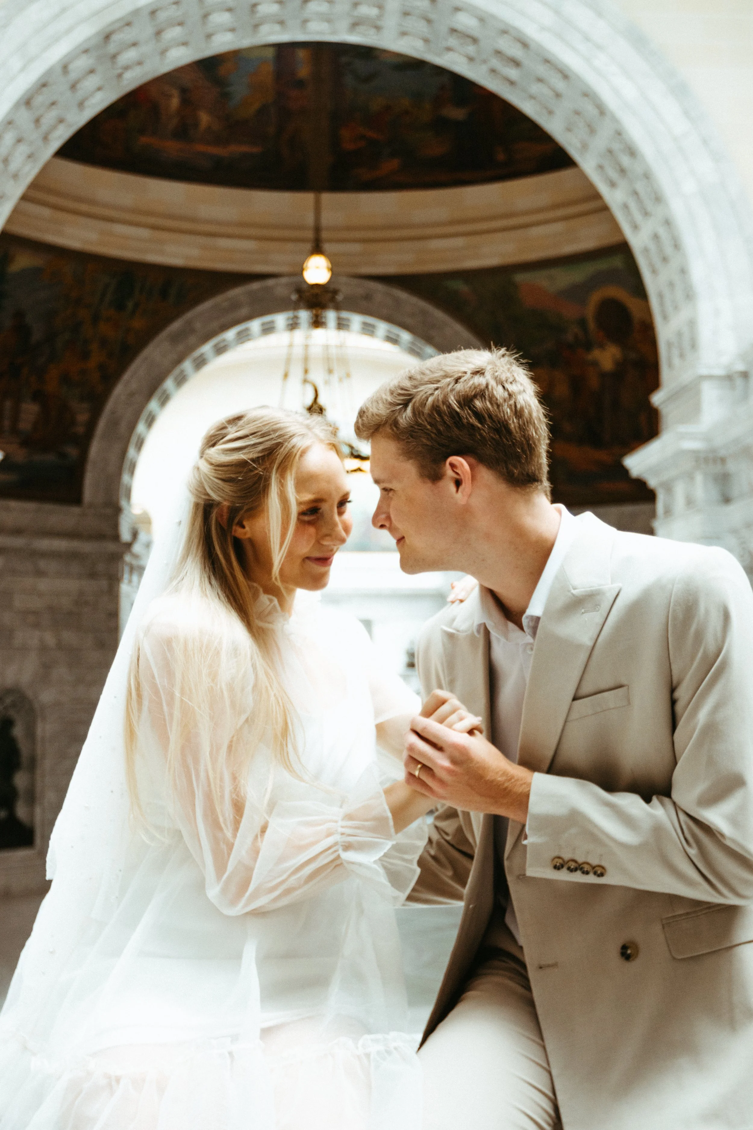 A bride and groom leaning close together inside a grand, ornate church, sharing an intimate moment during their wedding ceremony.