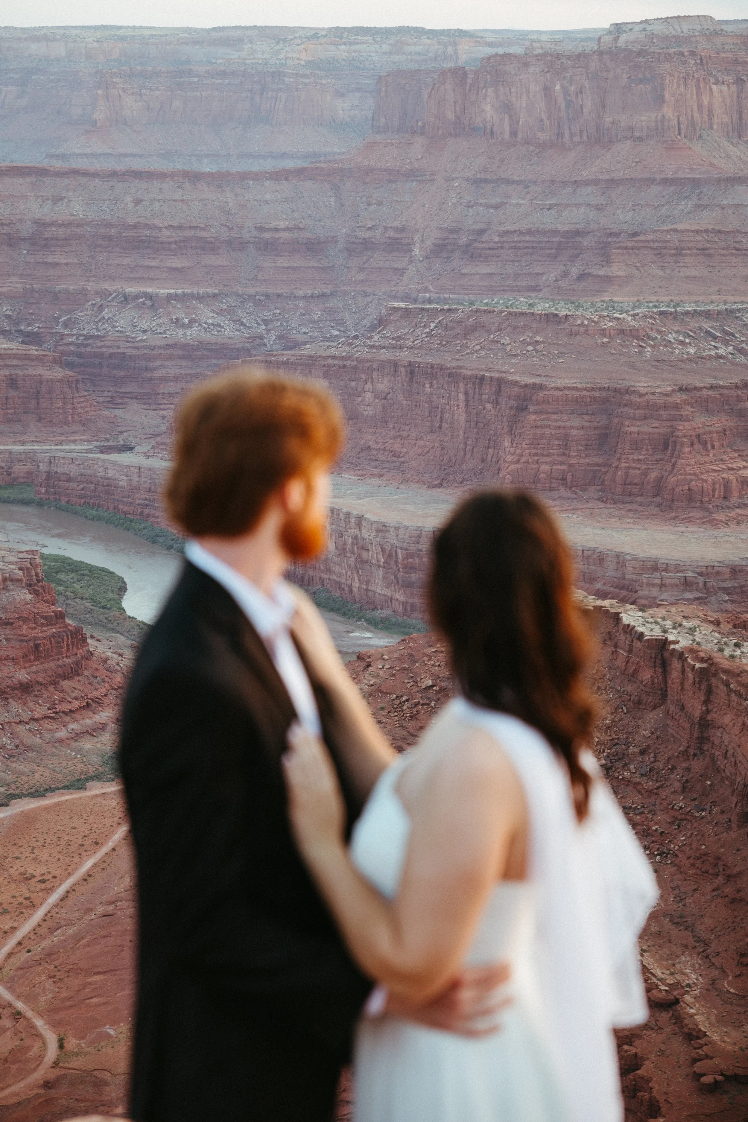 A couple in wedding attire standing close together with a view of the Grand Canyon in the background.
