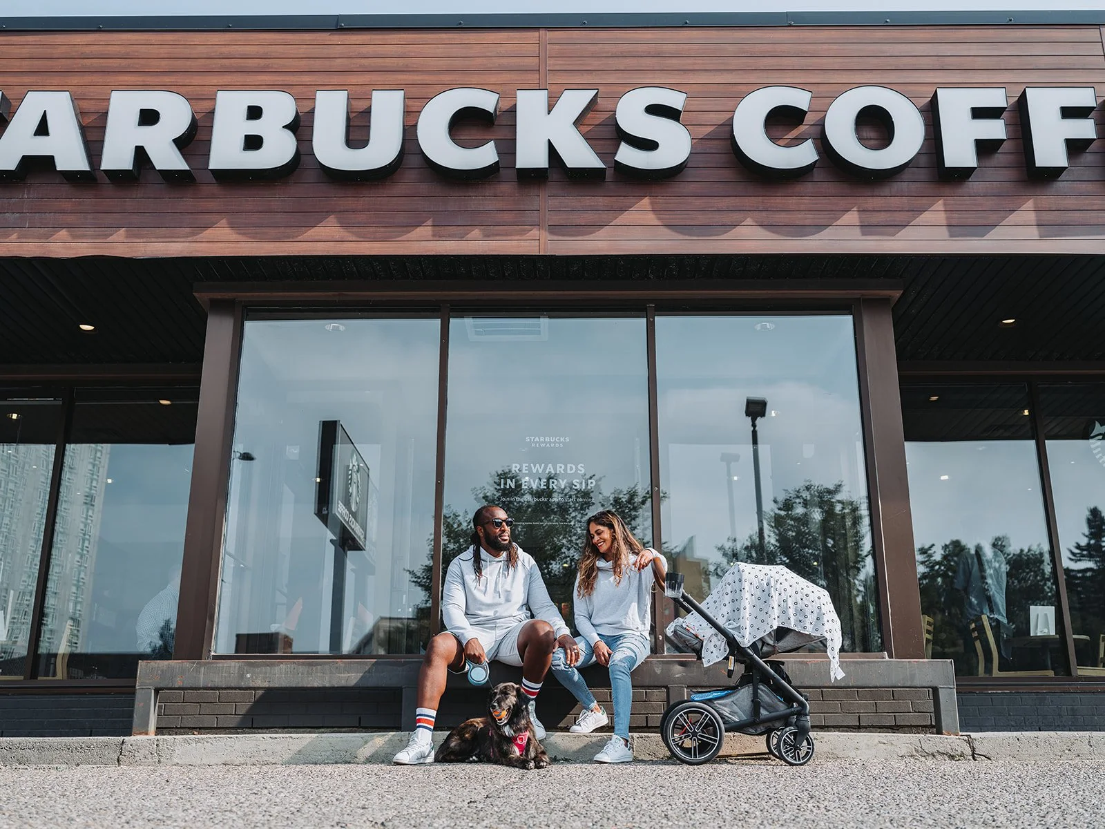 A couple sitting outside a Starbucks with a dog and stroller.
