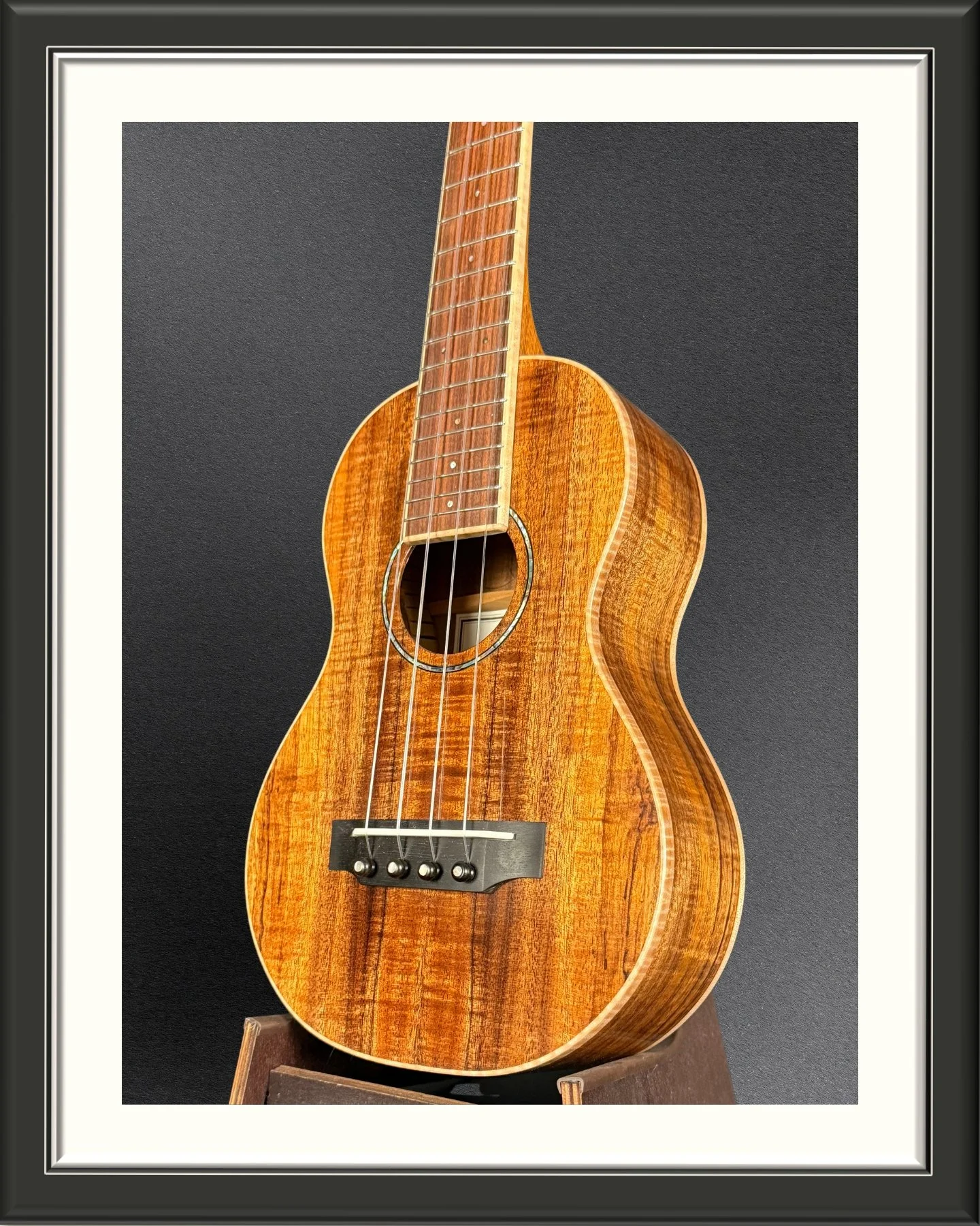 Front of the body, facing left, of a concert ukulele in Hawaiian Koa