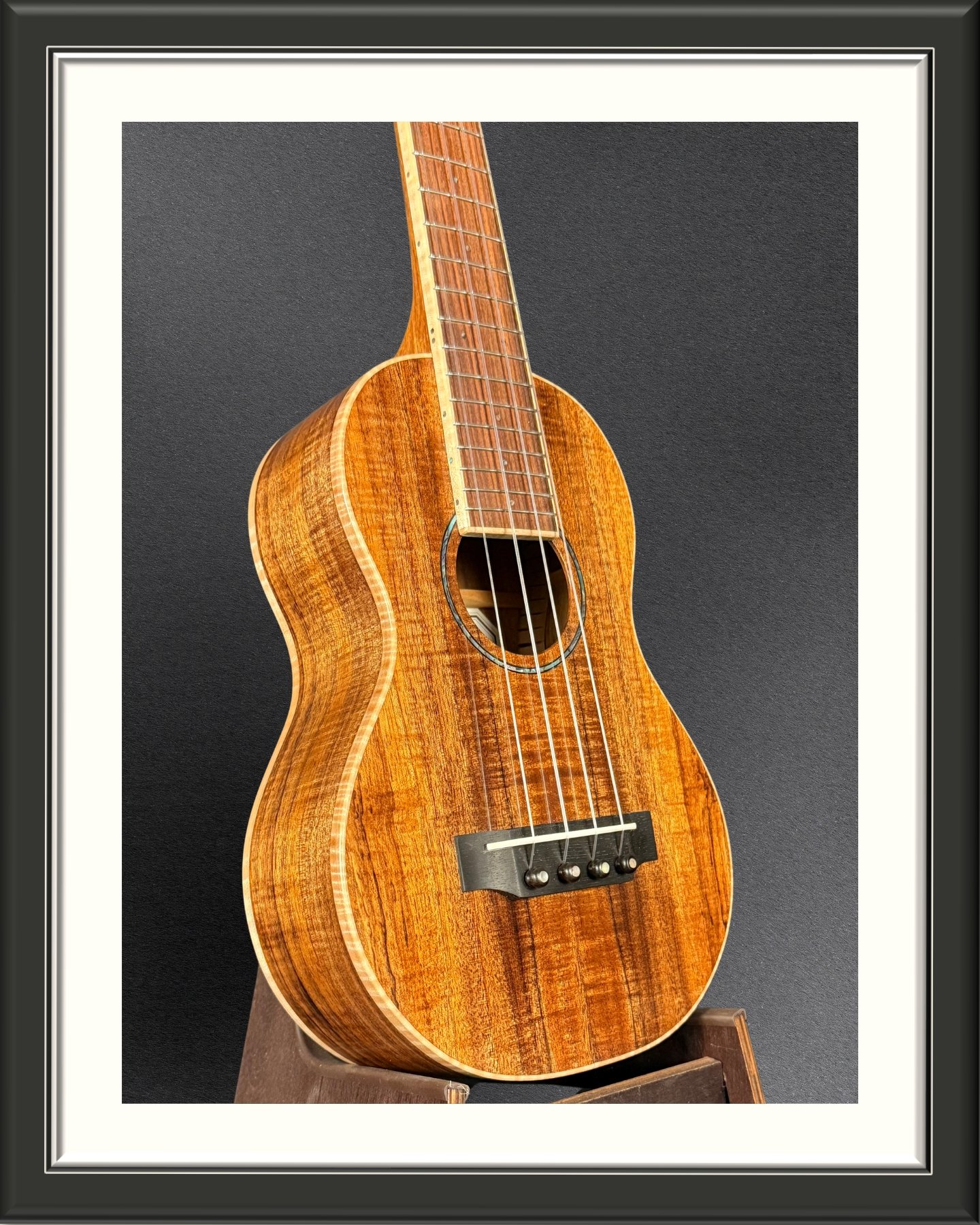 Front of the body, facing right, of a concert ukulele in Hawaiian Koa