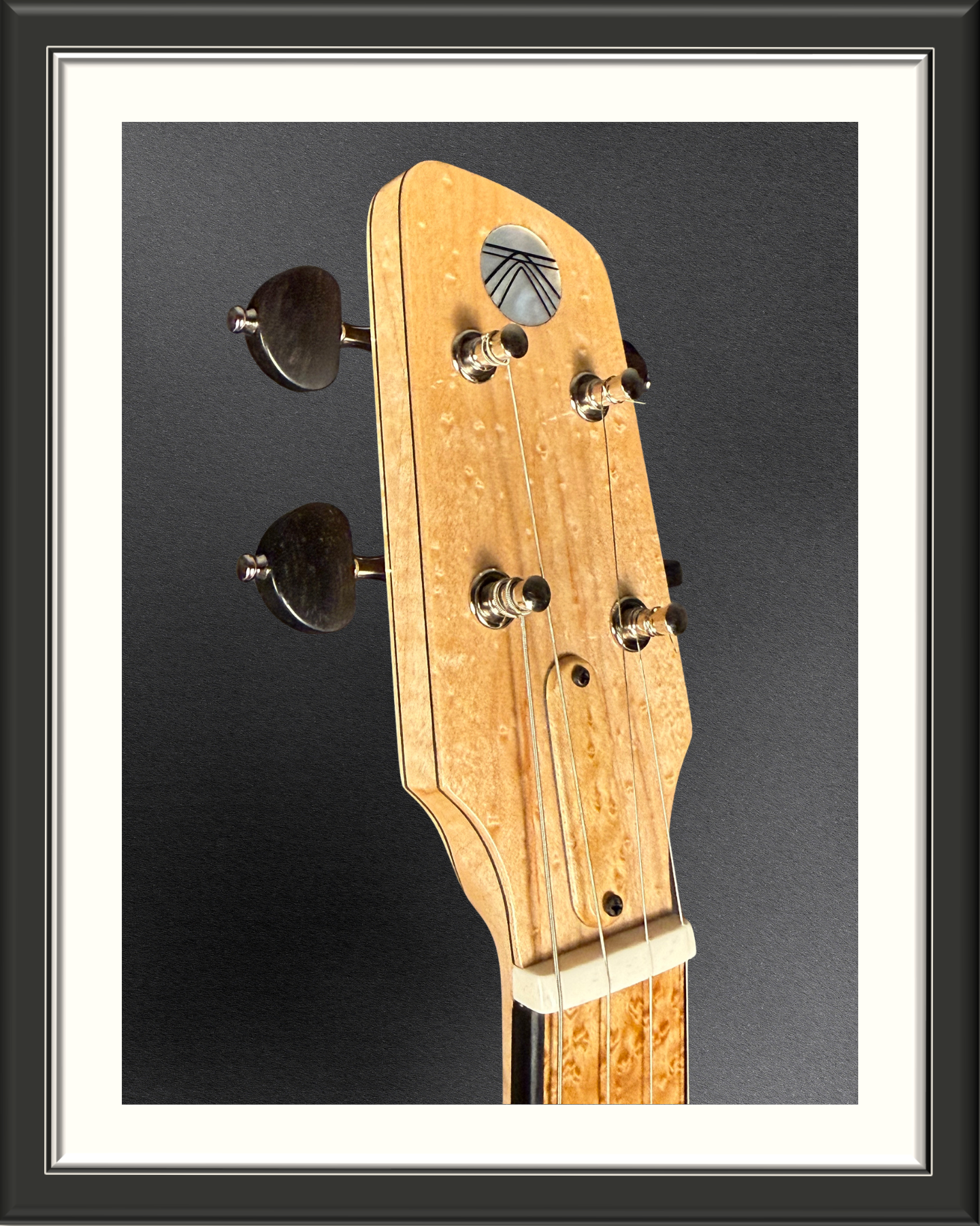 Close-up of the headstock at an angle with shockwave logo of the MachMachines Cuyler Model all-maple, hollow-body, electric baritone ukulele