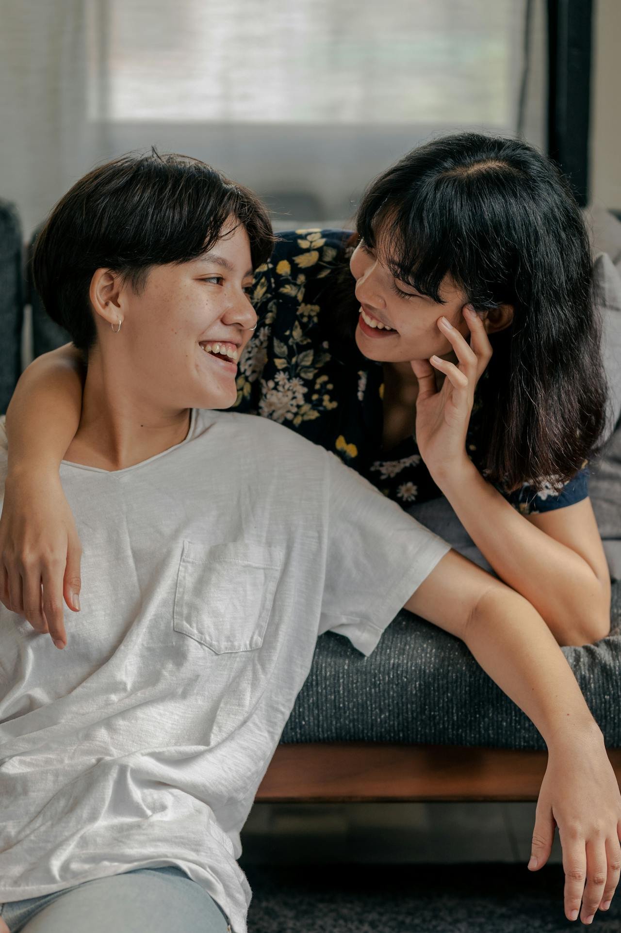 Two women smiling and embracing each other indoors.