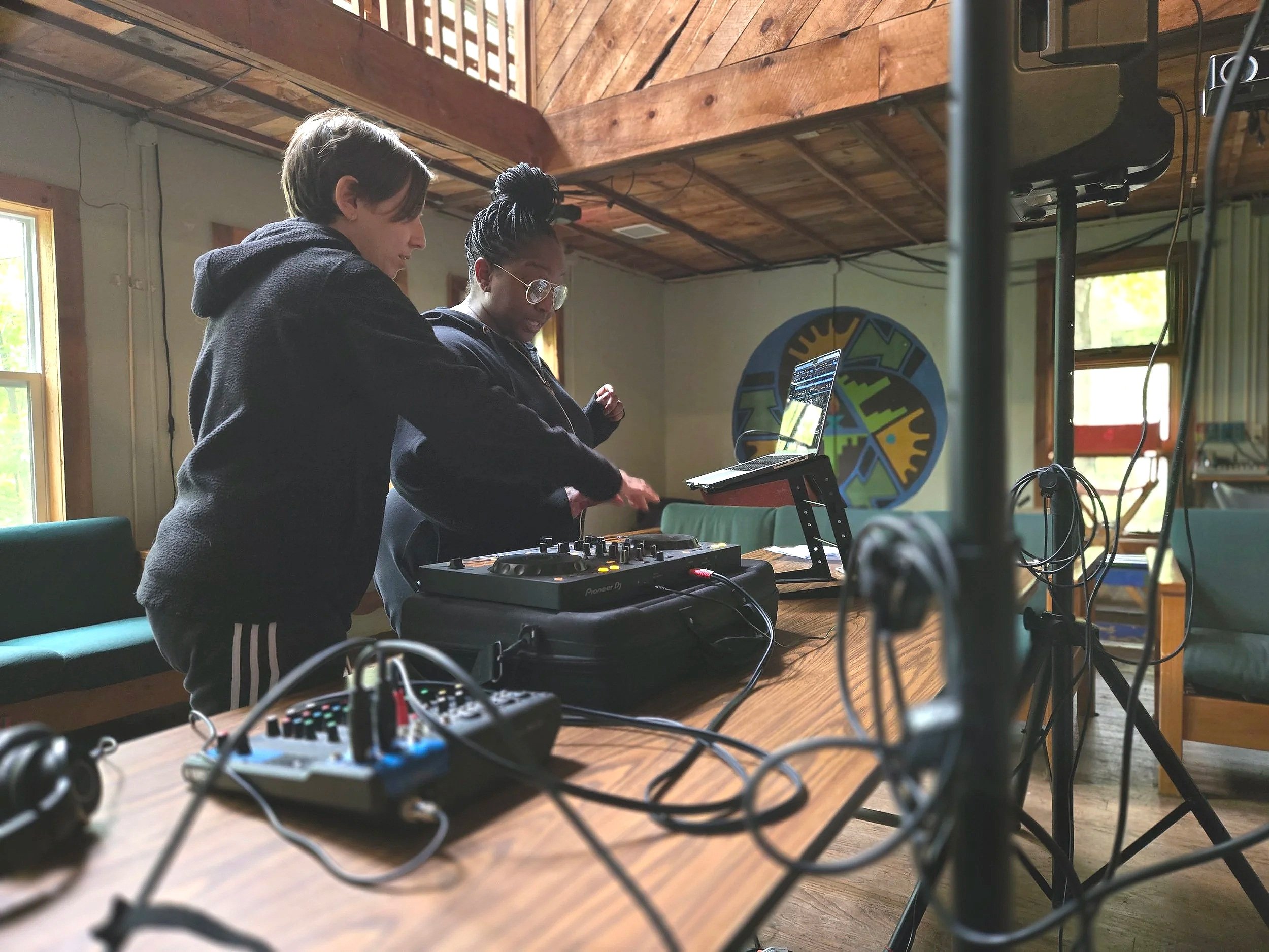 light skinned nonbrinary shows a Black woman how to use DJ equipment
