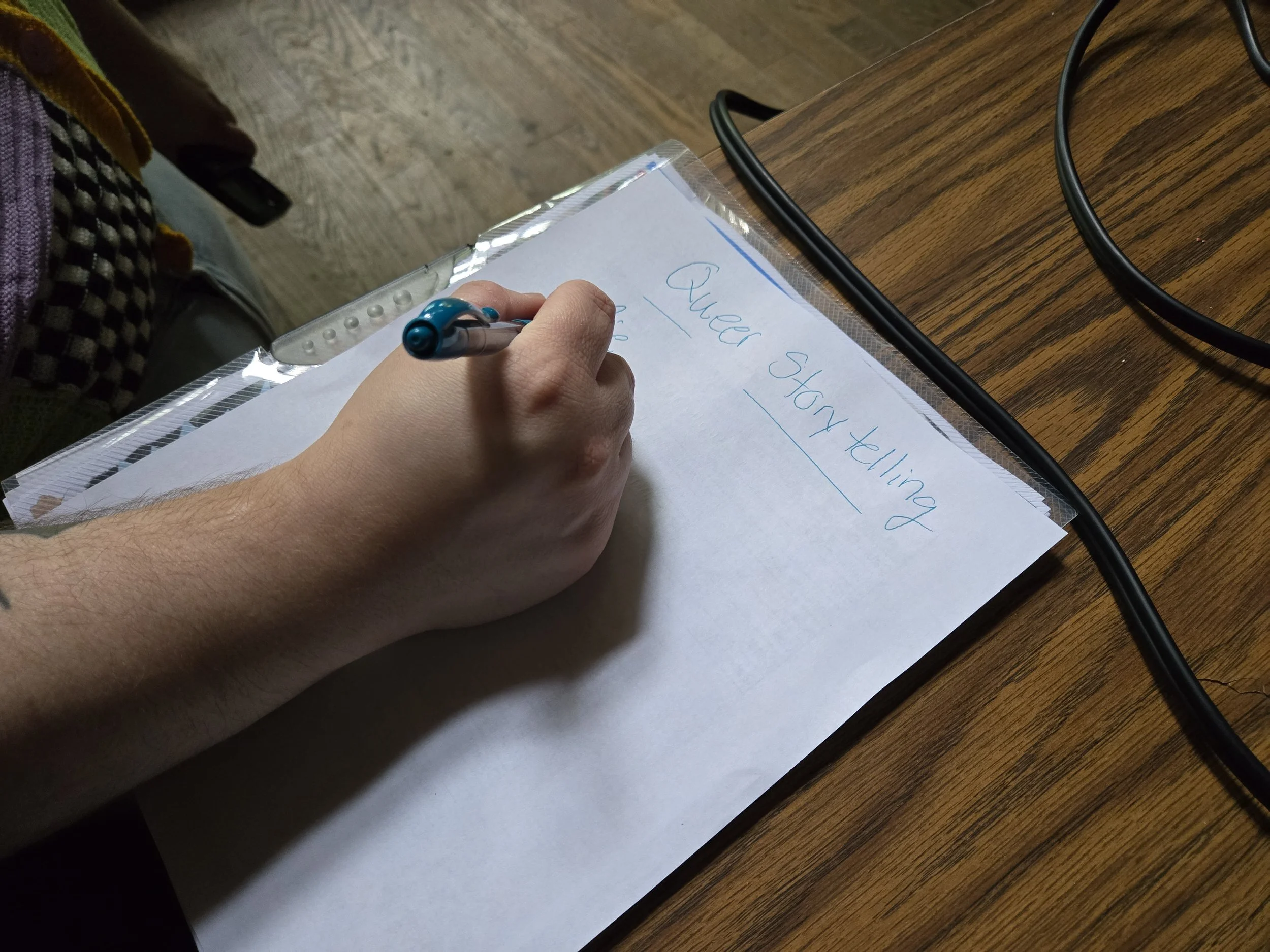 hand is writing on a paper that says queer storytelling