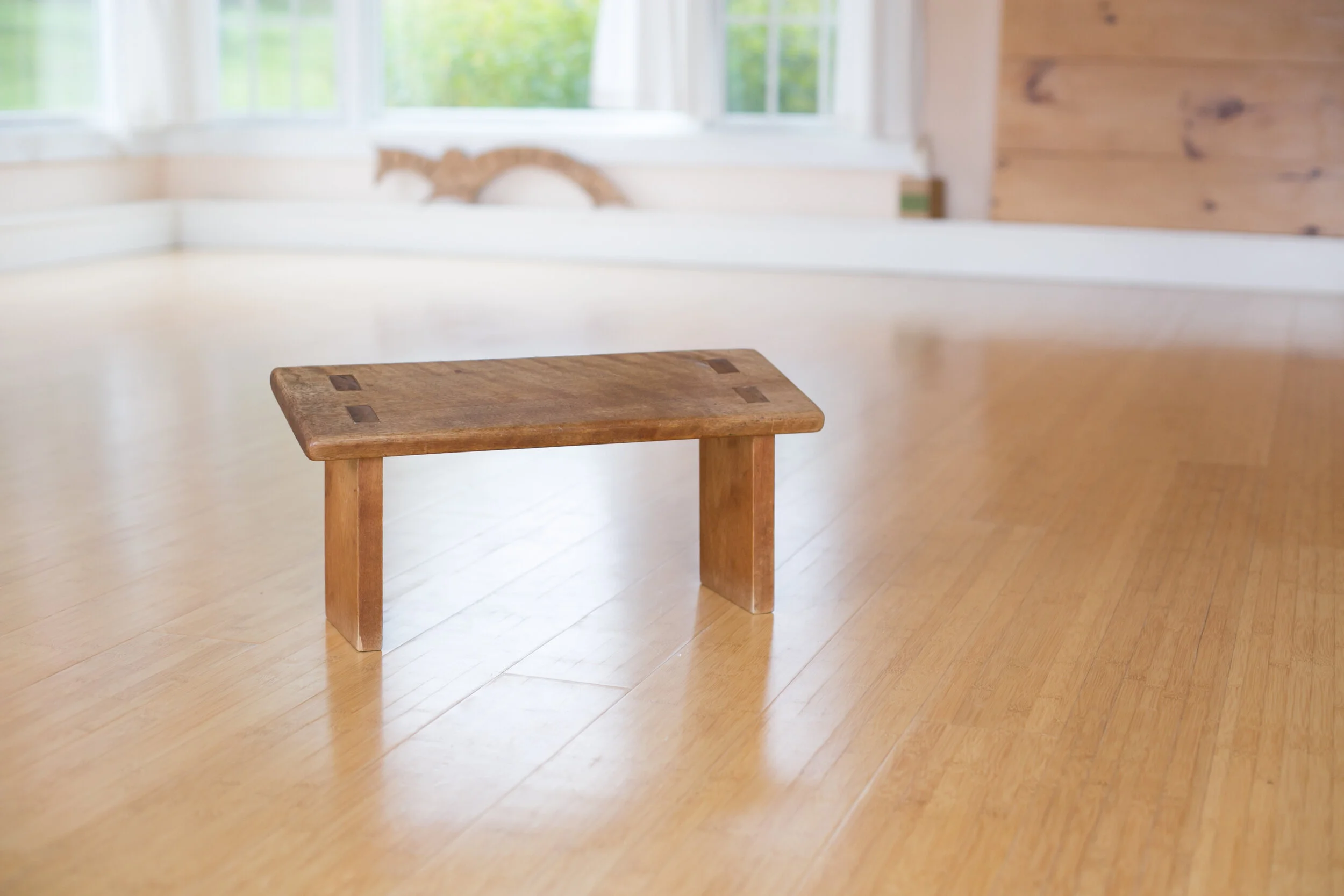 Wooden meditation bench on hardwood floor, ready with openness for someone to kneel into practice.