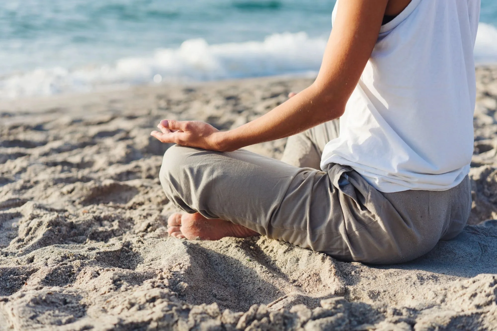 A woman meditating on the beach facing the ocean during a mindfulness practice