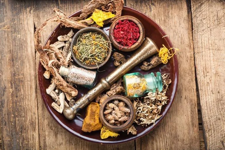 Colorful display of raw Chinese herbal medicines in a ceramic tray with individual vessels and a copper pestle at East-West Integrated Wellness