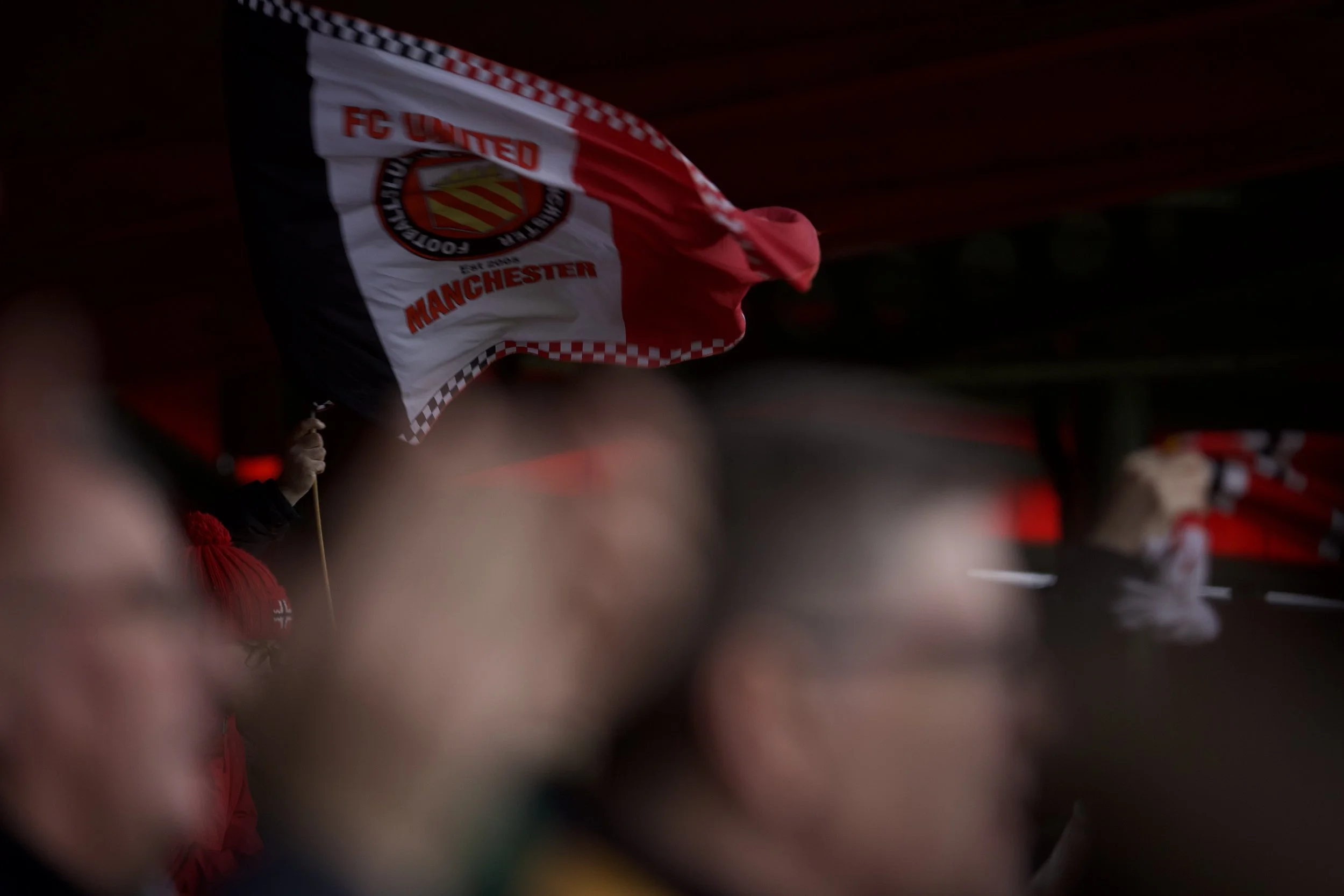Bandiera dell'FC United con i colori rosso, bianco e nero, visibile tra la folla di tifosi presenti a Broadhurst Park