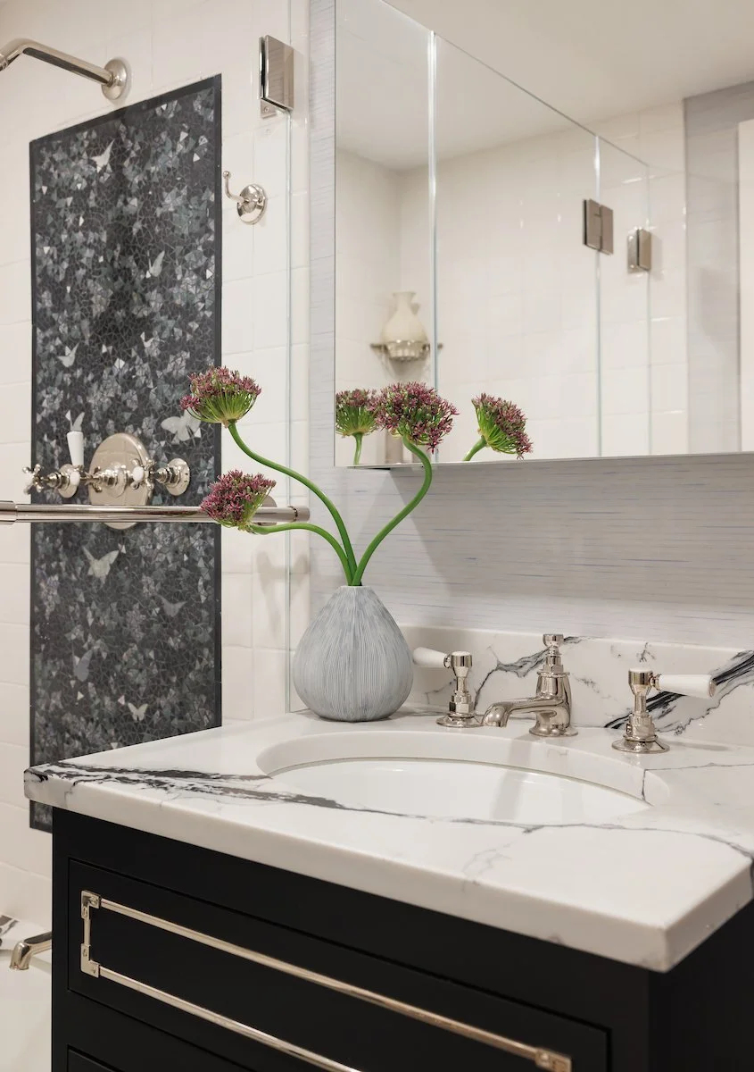 Custom black bathroom vanity with white stone countertop, polished fixtures, and dramatic decorative stone backsplash in Manhattan.