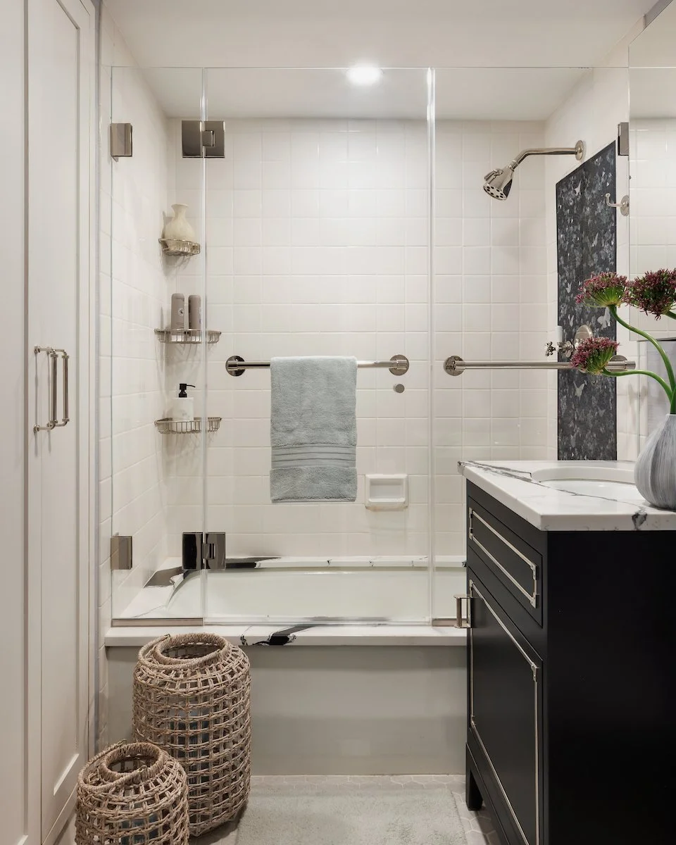 Sophisticated Manhattan bathroom renovation featuring glass shower enclosure, black vanity, white tile, and decorative stone accents.