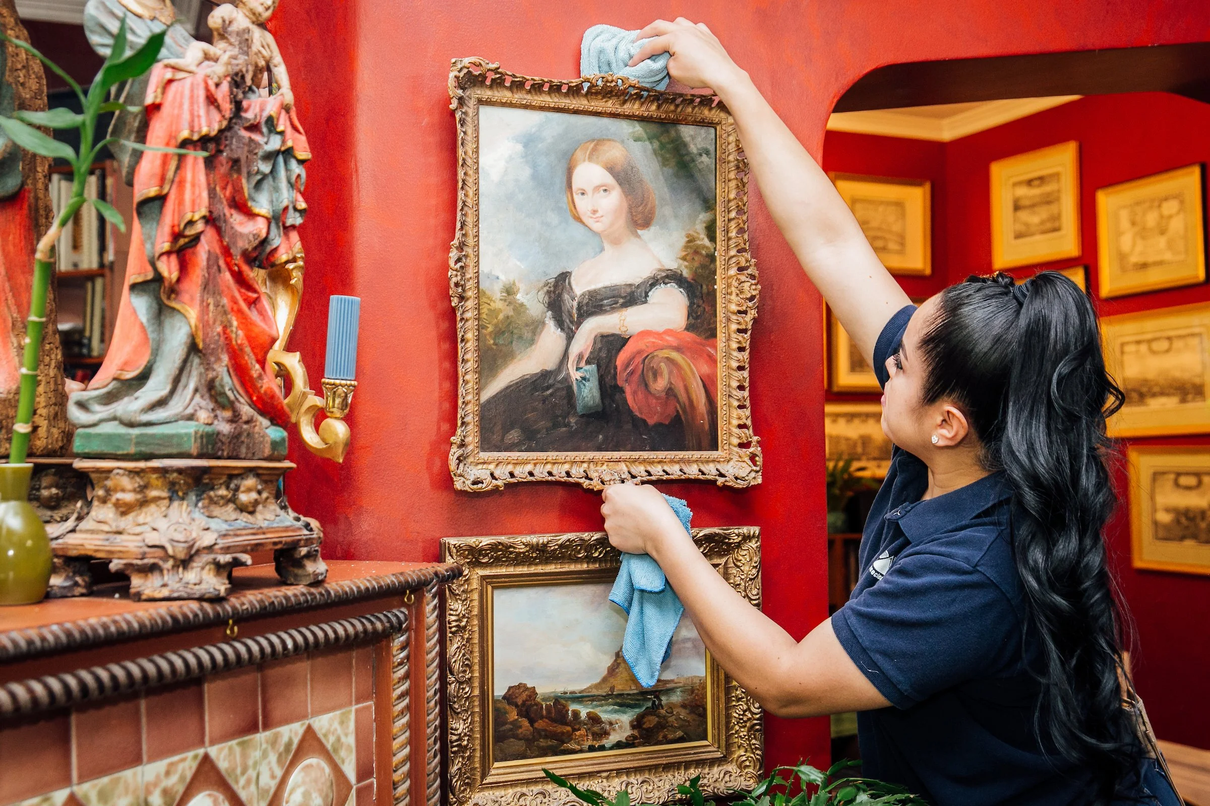 Woman cleans the frames of an old painting in a colorful home