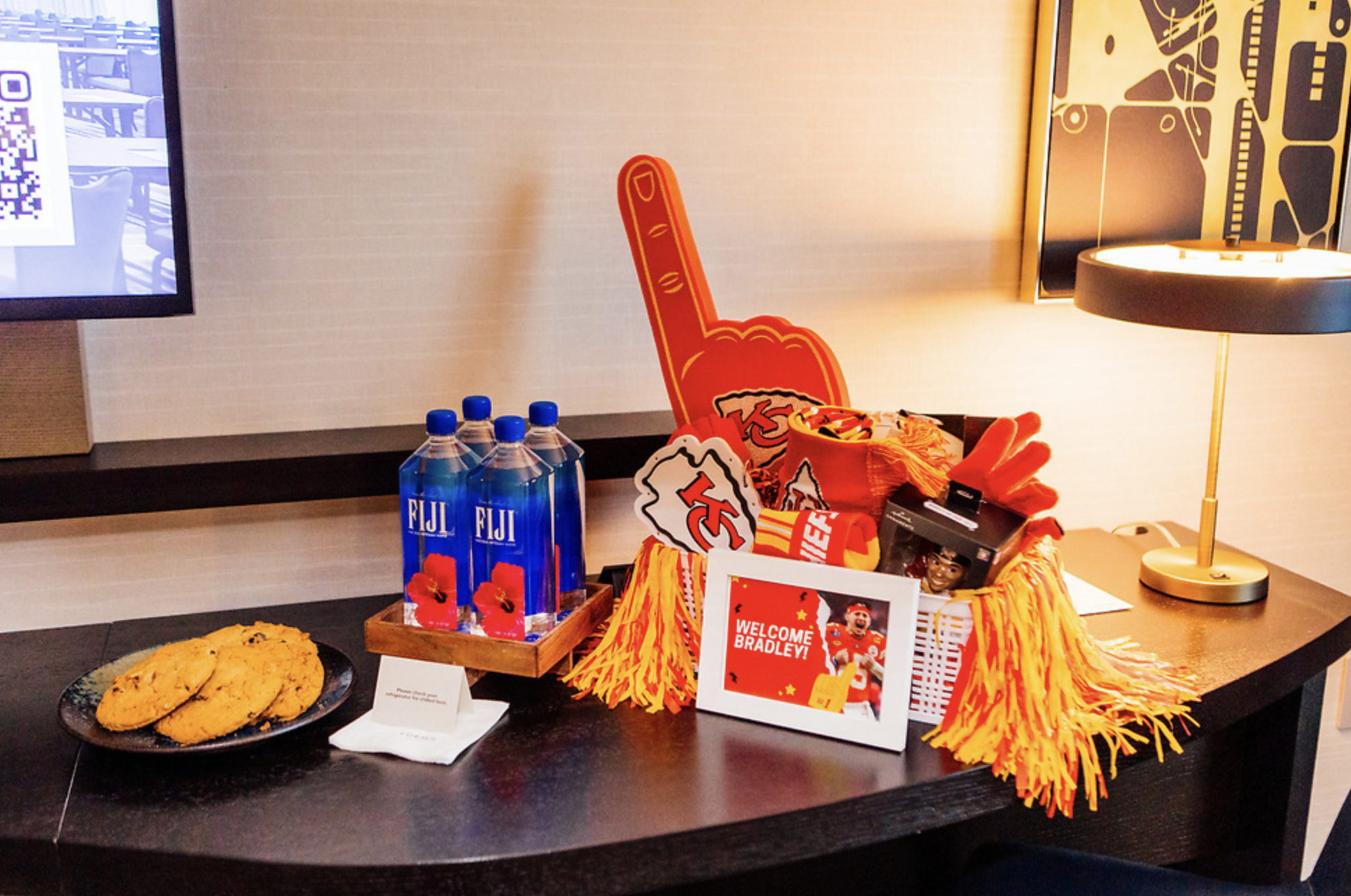 A plate of cookies, waters, and basket of Kansas City Chiefs Gear sits on Hotel Table