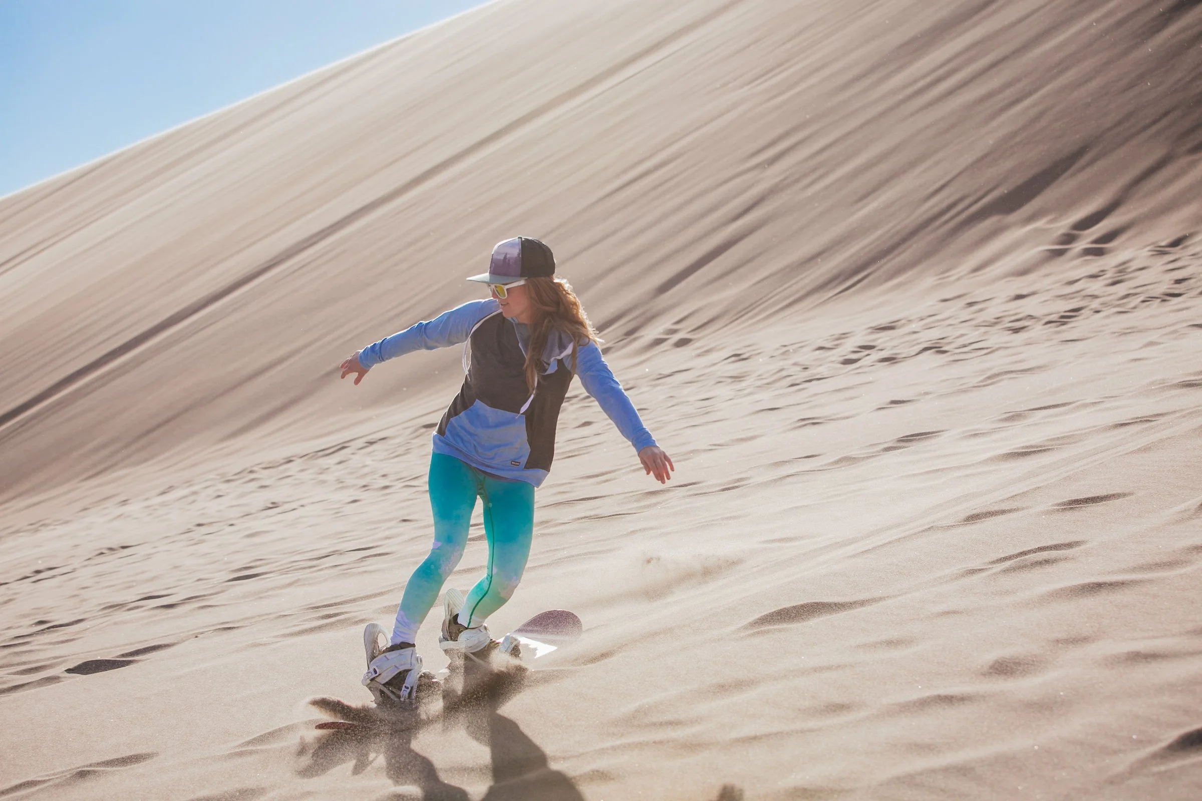 Woman boards down great sand dunes modeling Belong Designs sweatshit