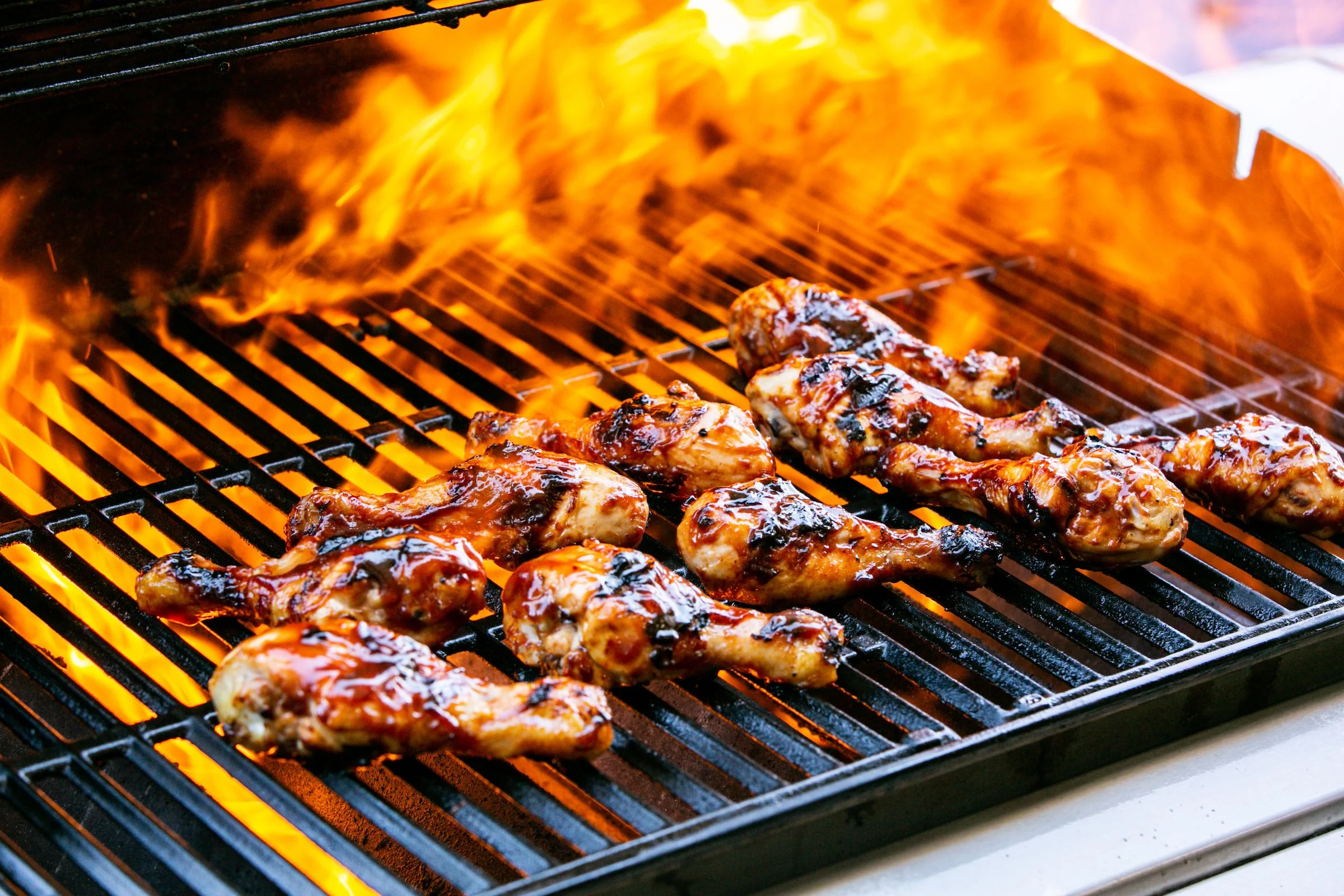 BBQ chicken legs cook on grill surrounded by flames