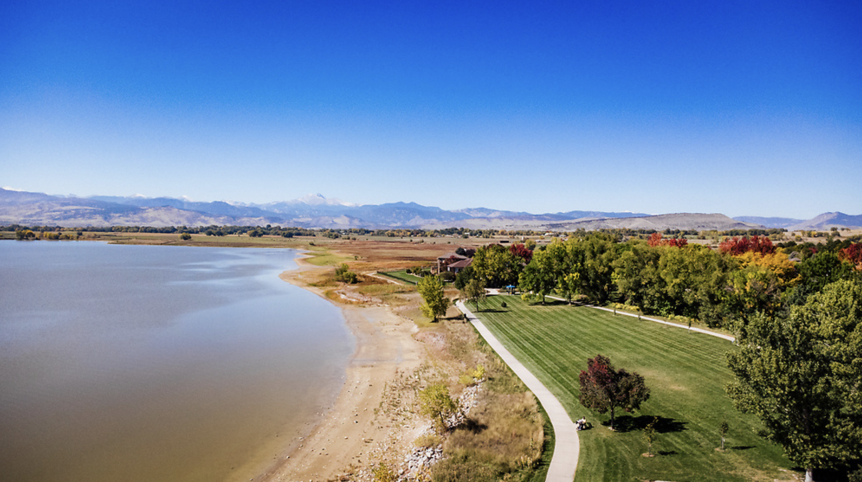 Drone shot of a park running alongside a lake with the mountains in the background