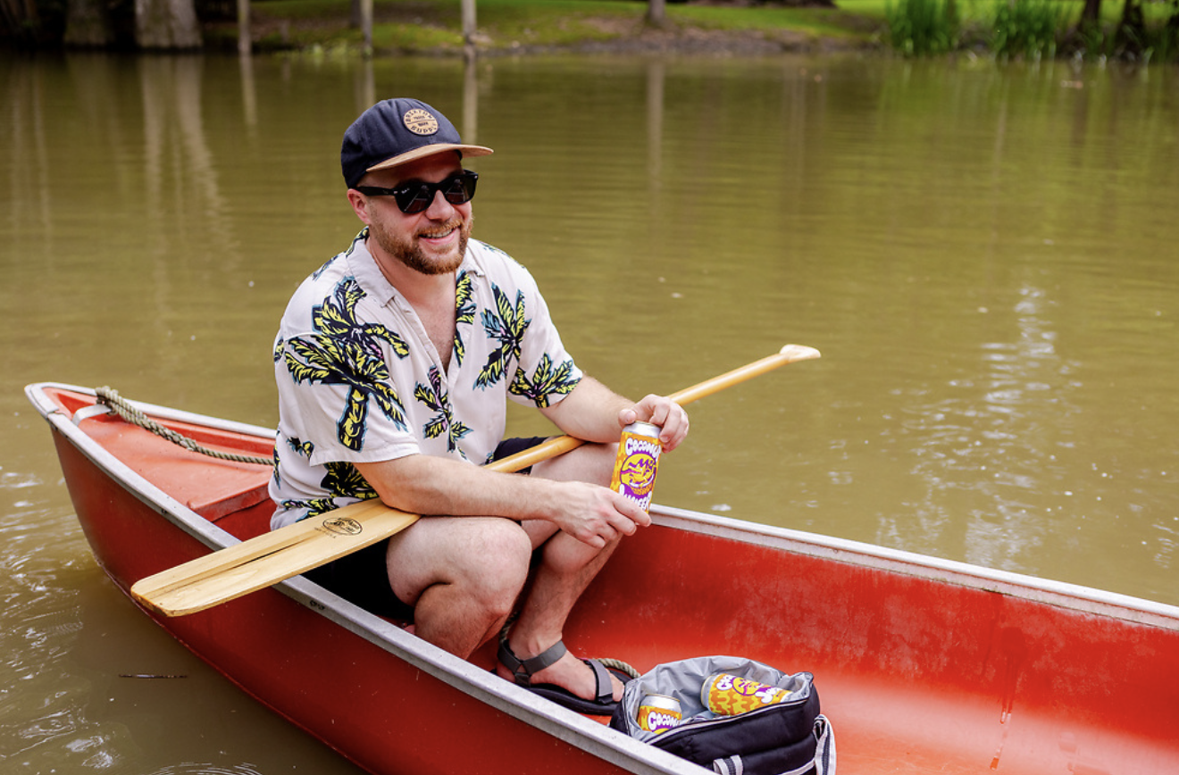 Man sits in a canoe with his cooler of beers and is opening one
