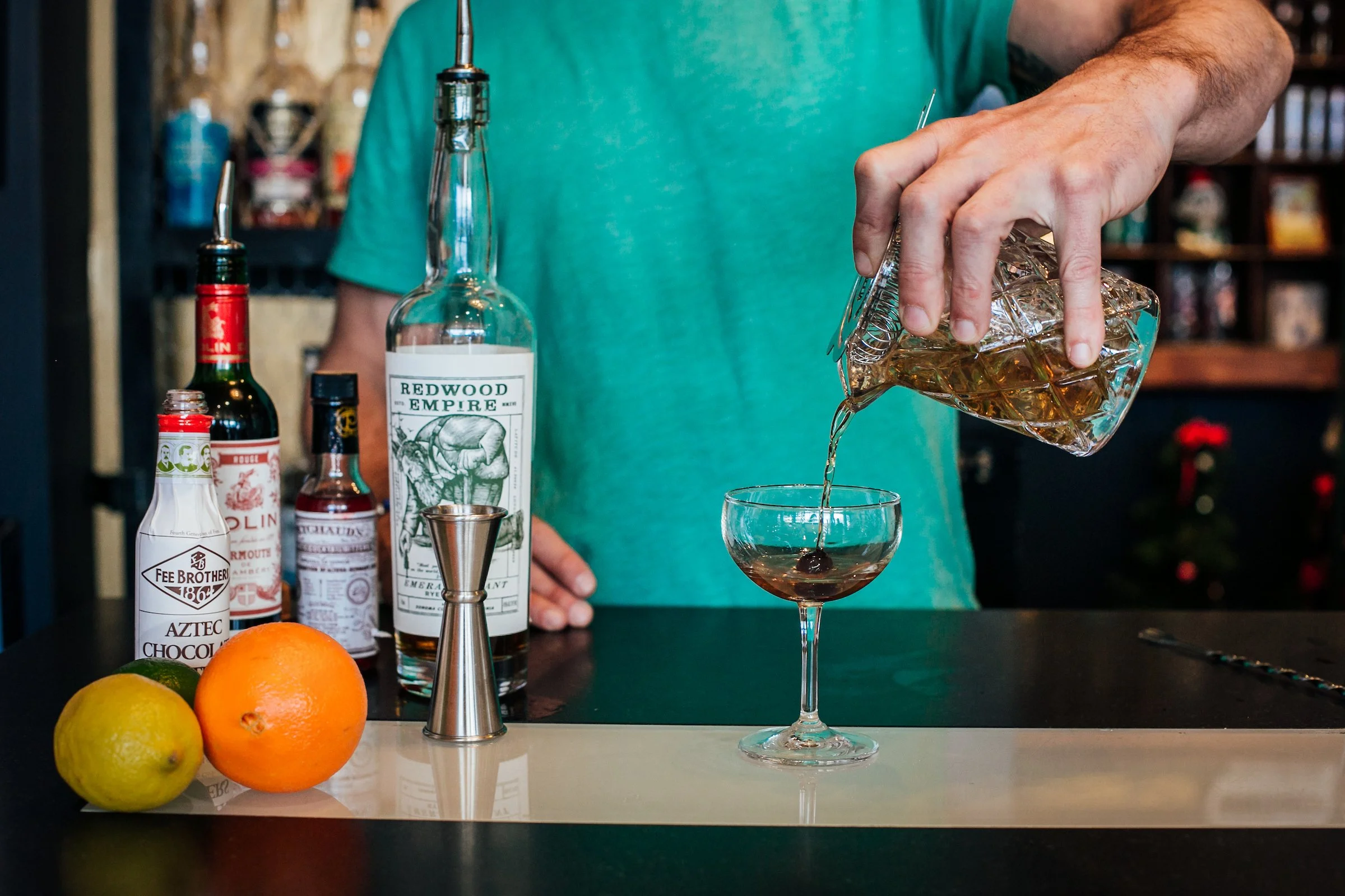 Pouring drink into glass with bottles of ingriedients behind it