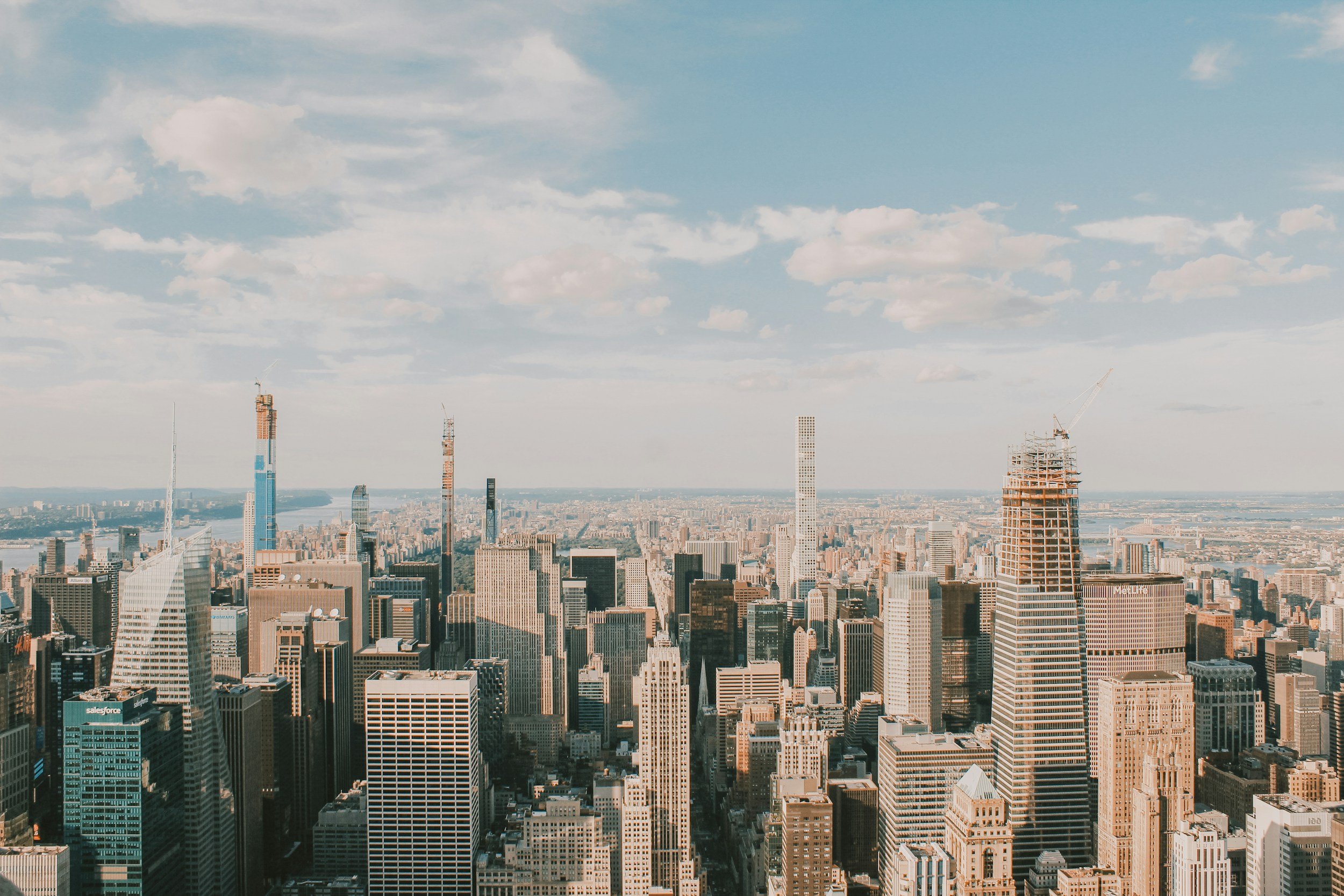 A city skyline with numerous tall skyscrapers, some under construction, under a partly cloudy sky.