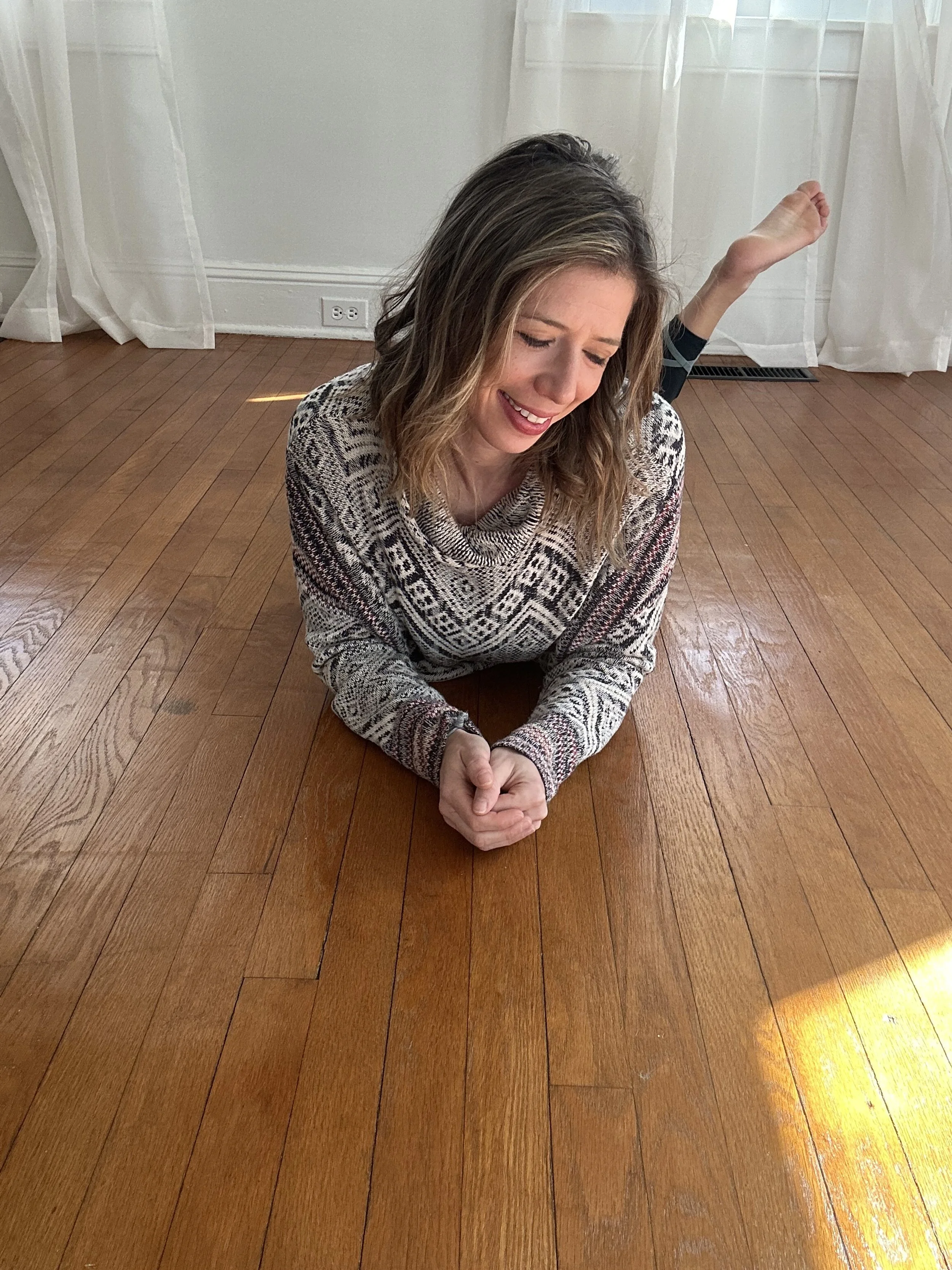 Woman lying on a wooden floor, crying with a pained expression, wearing a patterned sweater.