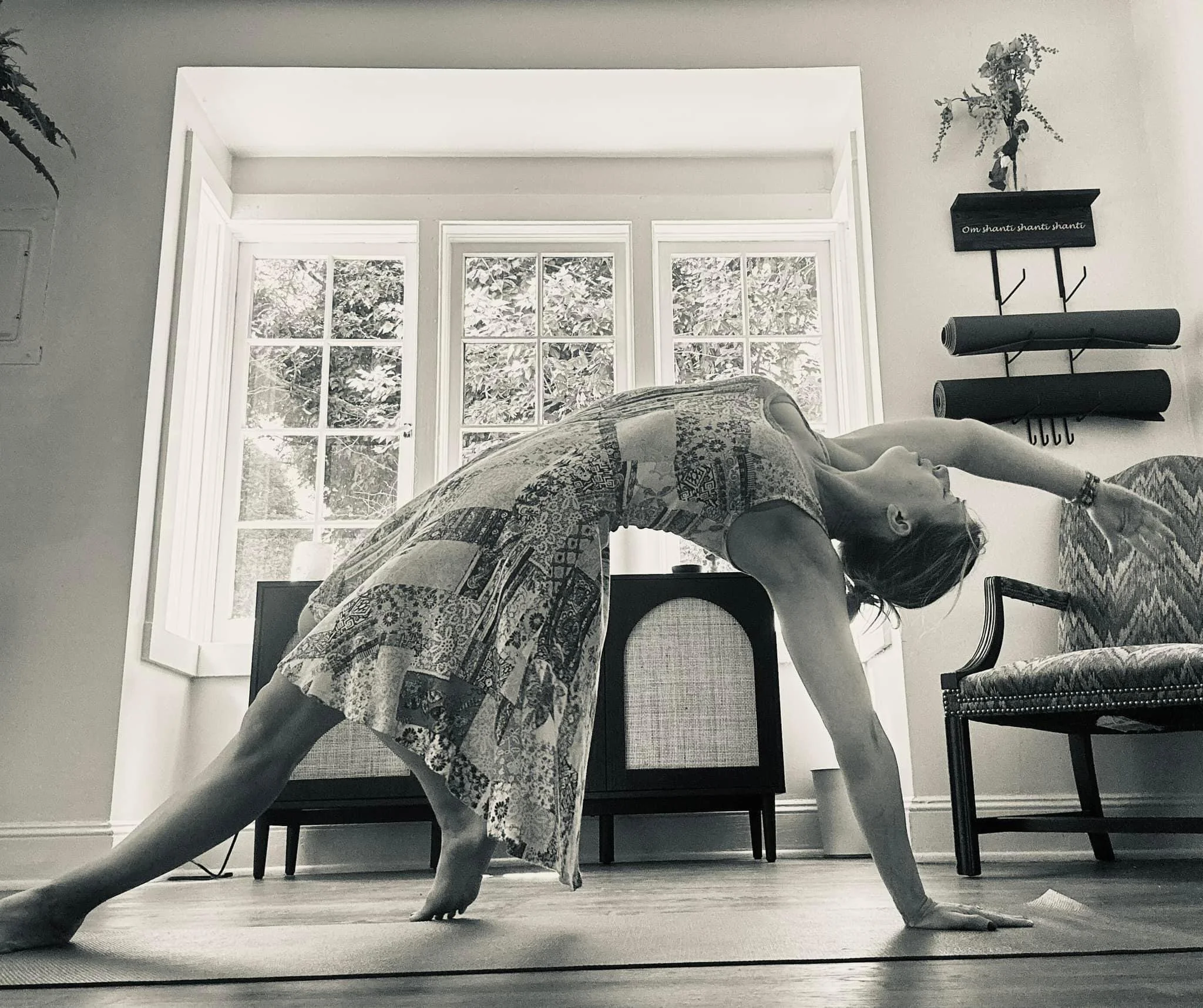A woman practicing yoga in a sunlit room, performing a downward dog pose on a yoga mat.