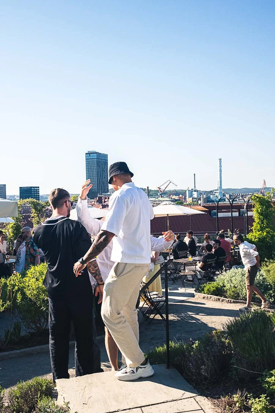 People enjoying a rooftop outdoor gathering with cityscape in the background on a sunny day.