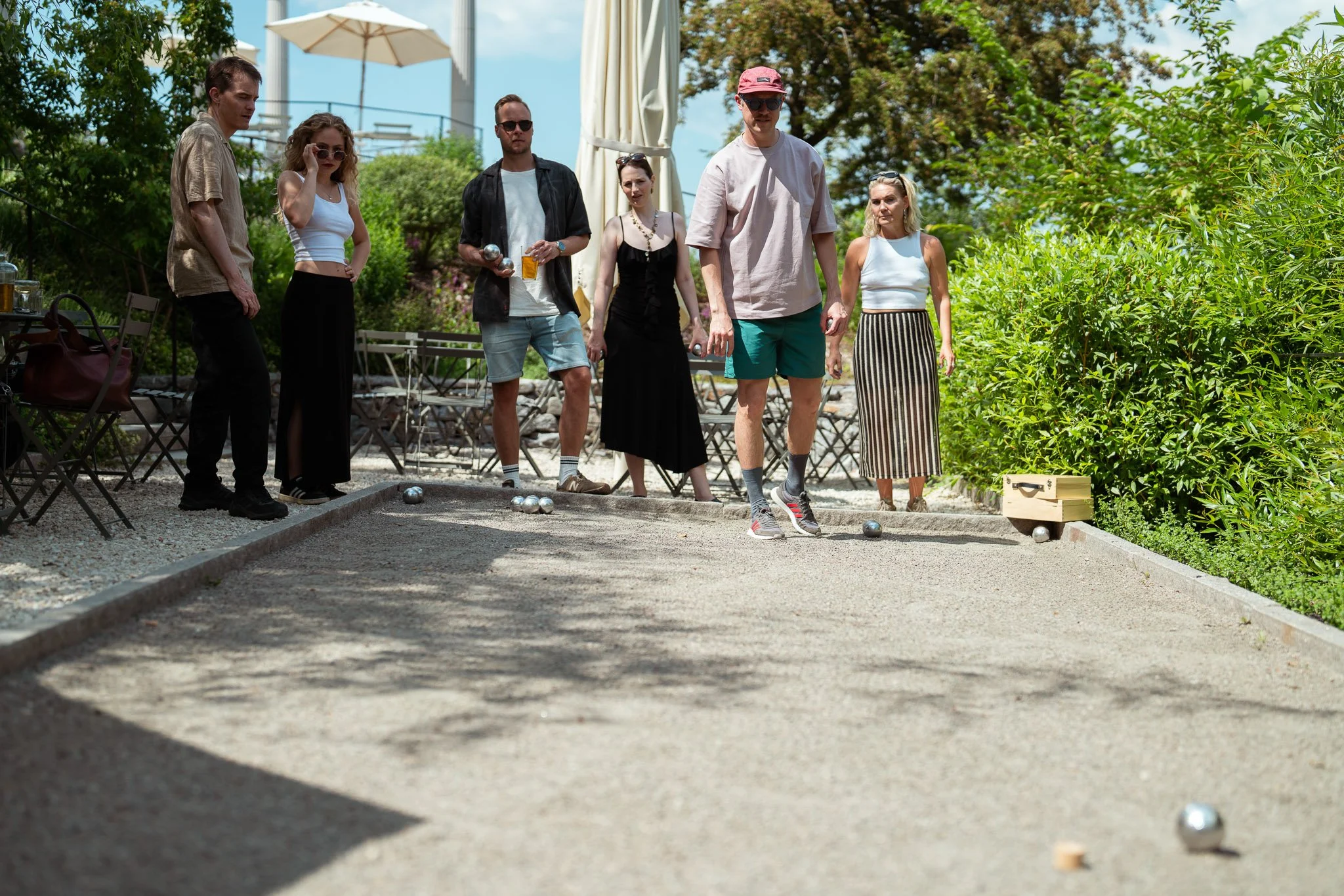 People playing outdoor bocce ball on a sunny day surrounded by greenery.