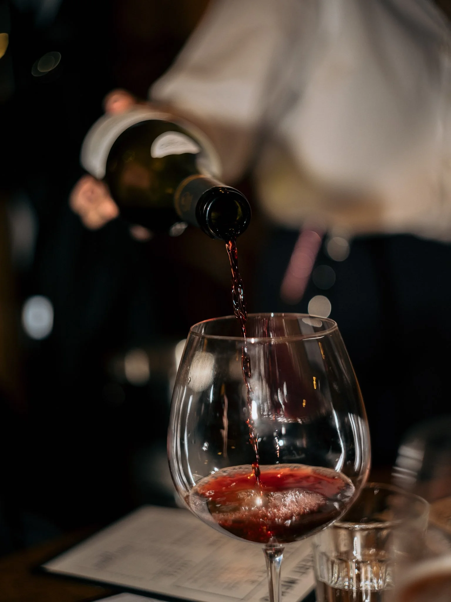 Person pouring red wine into a glass in a dimly lit setting.