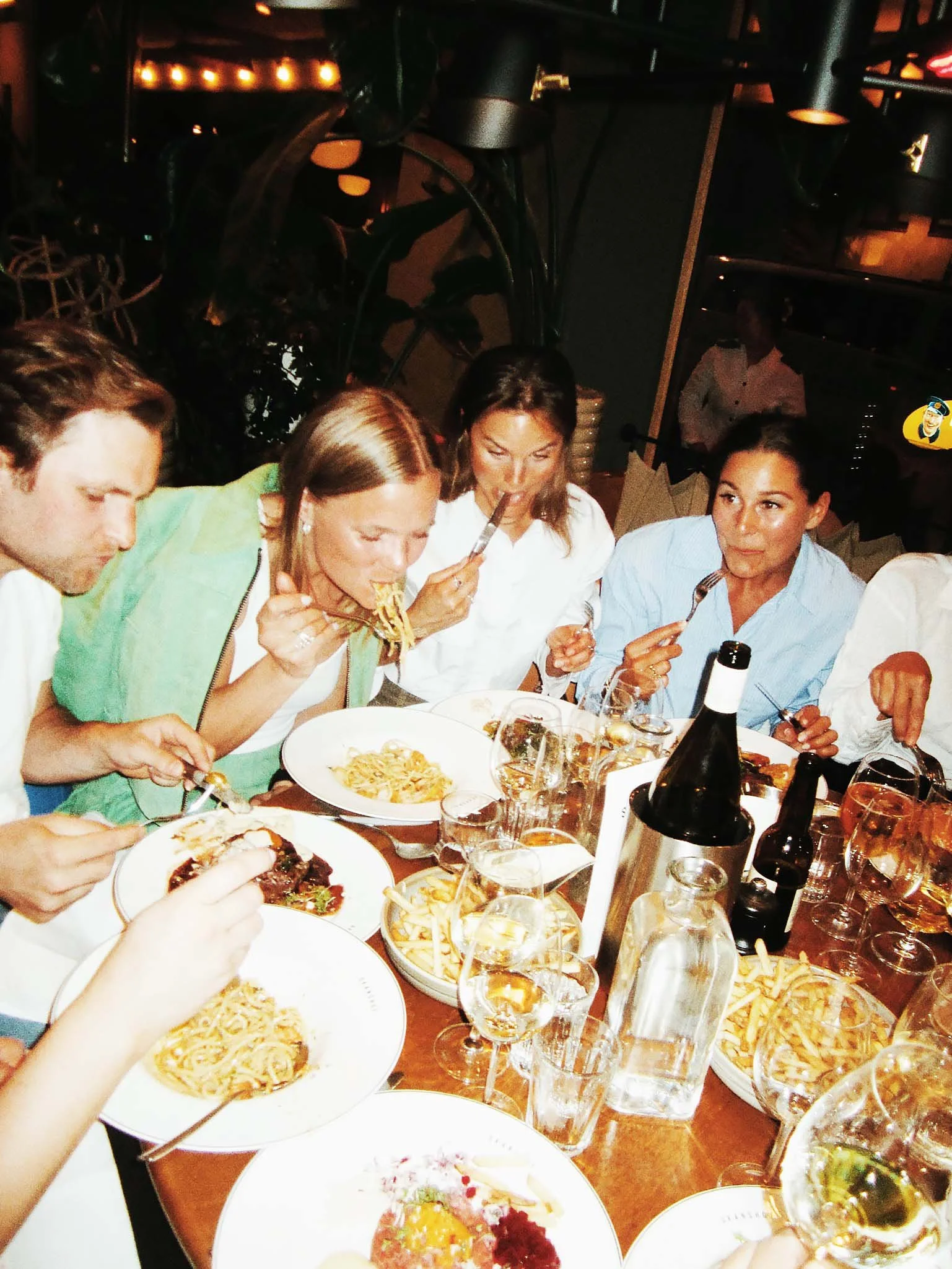 People at a dinner table enjoying pasta and drinks in a restaurant.
