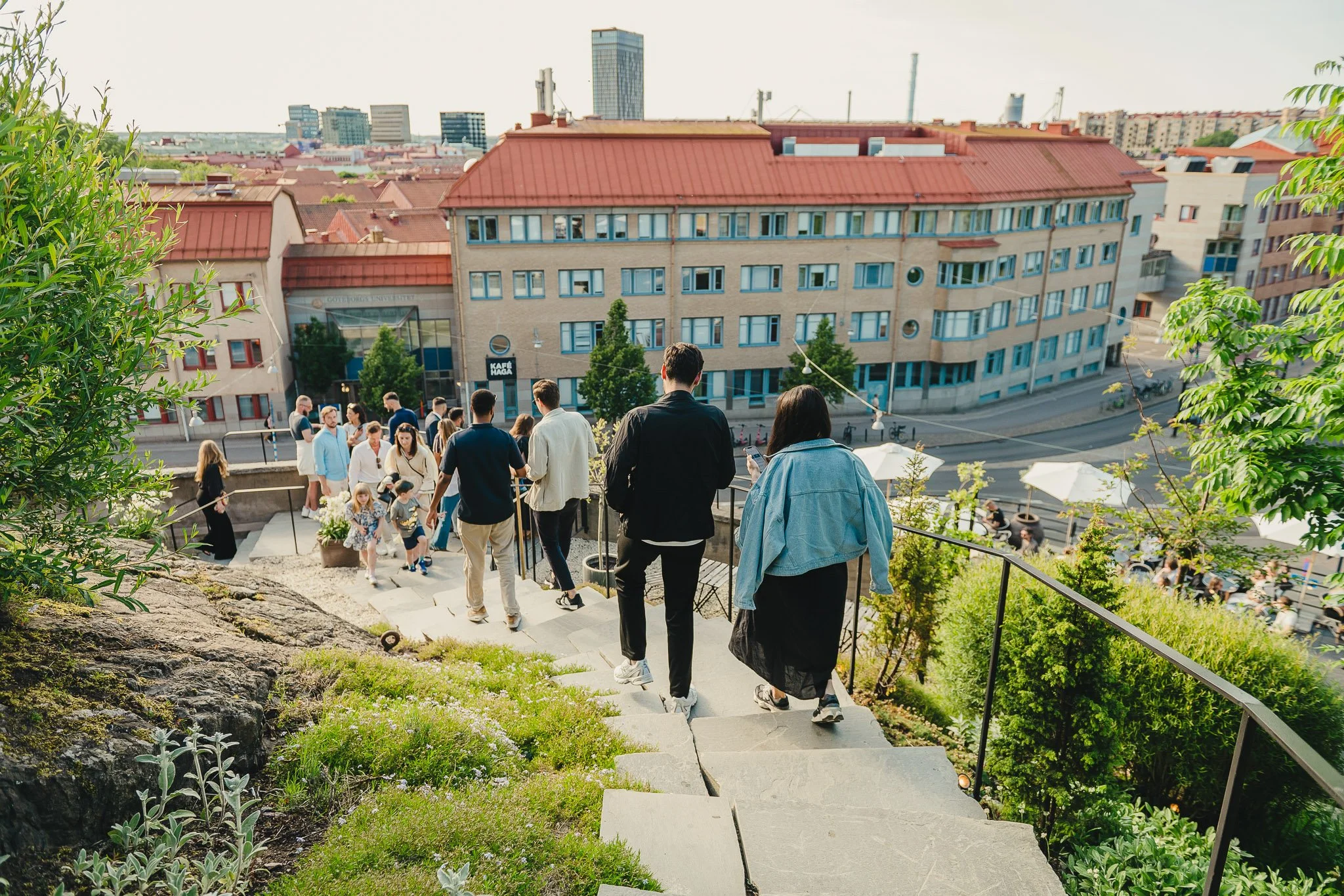A group of people walking up outdoor stairs on a hillside in an urban area with buildings and cityscape in the background.