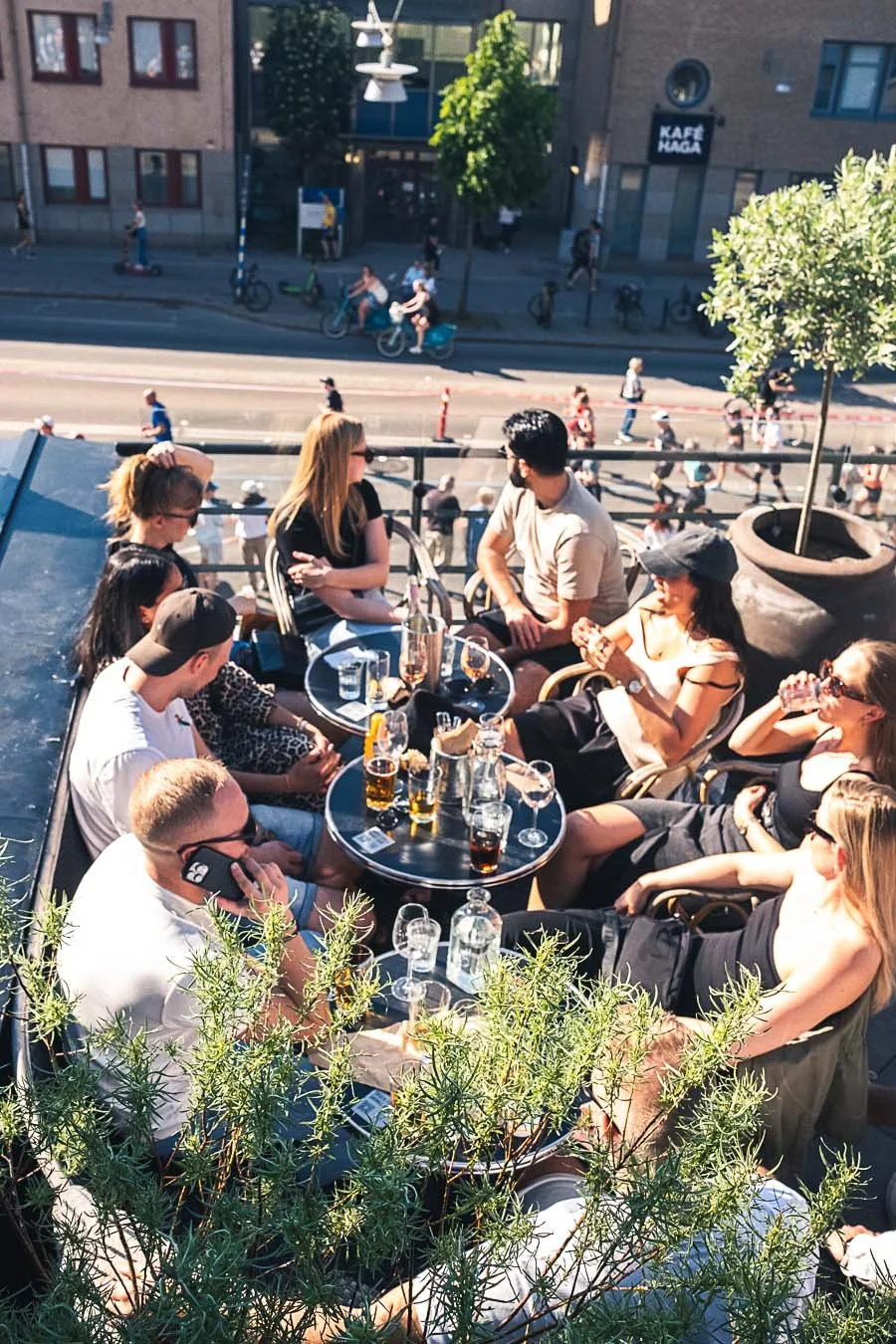 People sitting on an outdoor balcony with glasses and bottles on the table, overlooking a busy street with pedestrians and cyclists.