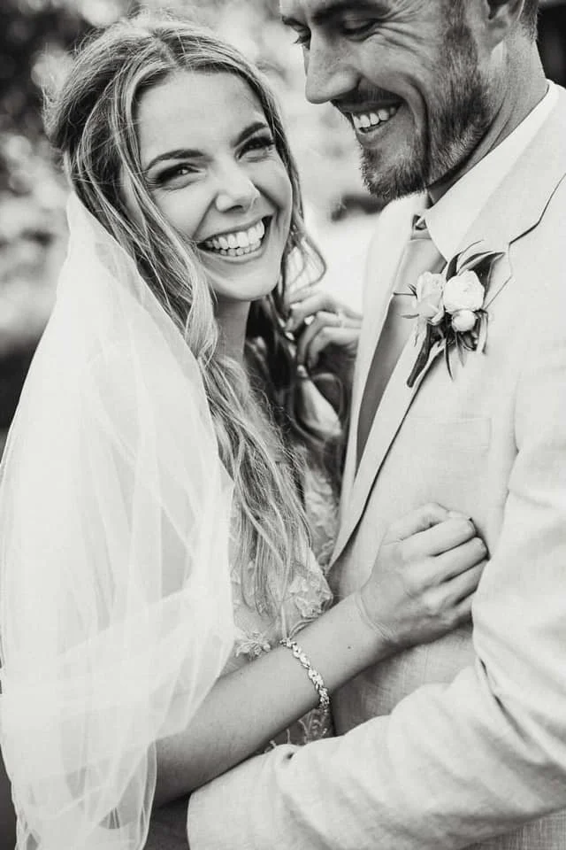Black and white photo of a smiling bride and groom holding hands, close together outdoors.