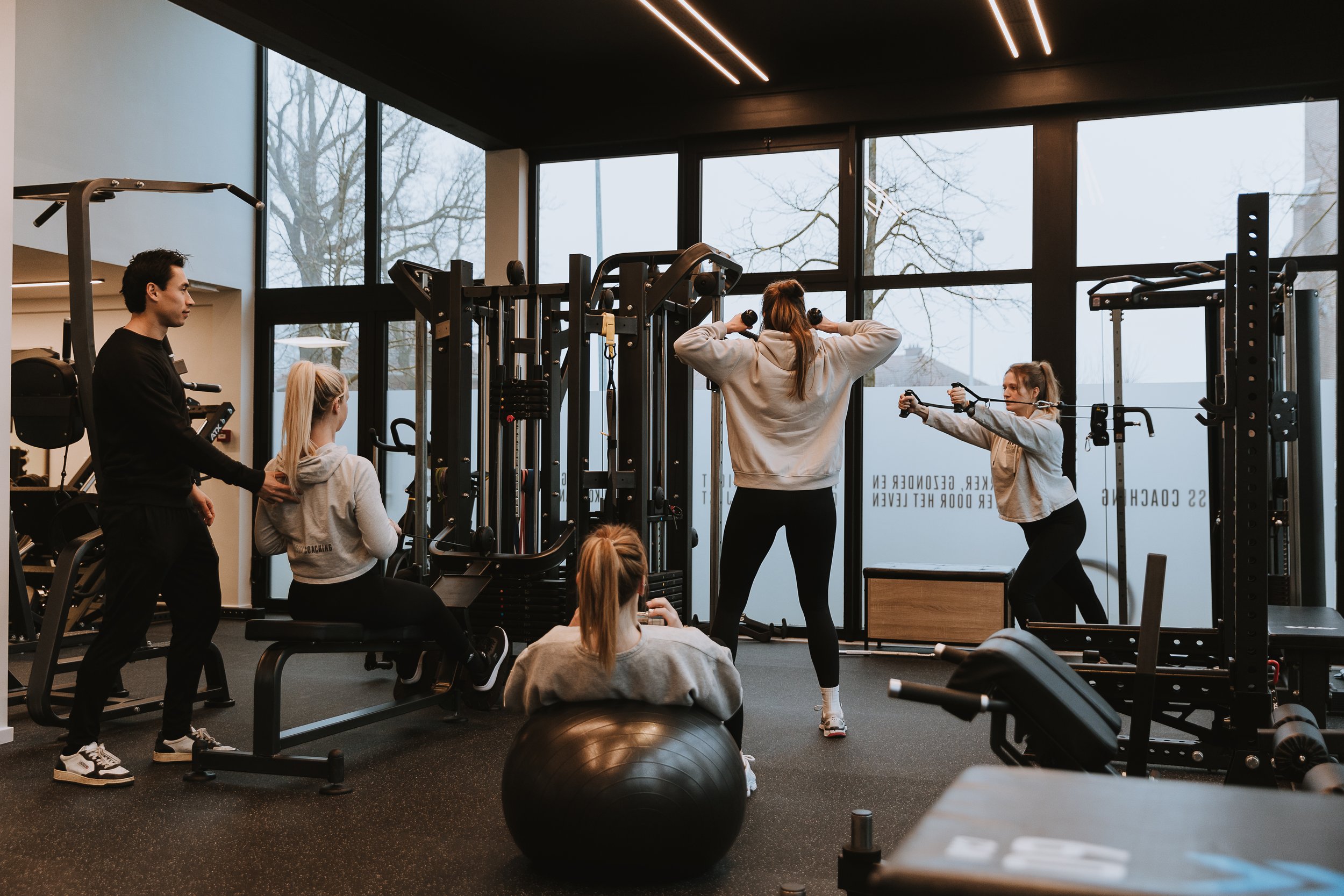 Mensen trainen in een sportschool met krachtapparaten en gewichten samen met een personal coach en in small-group training.