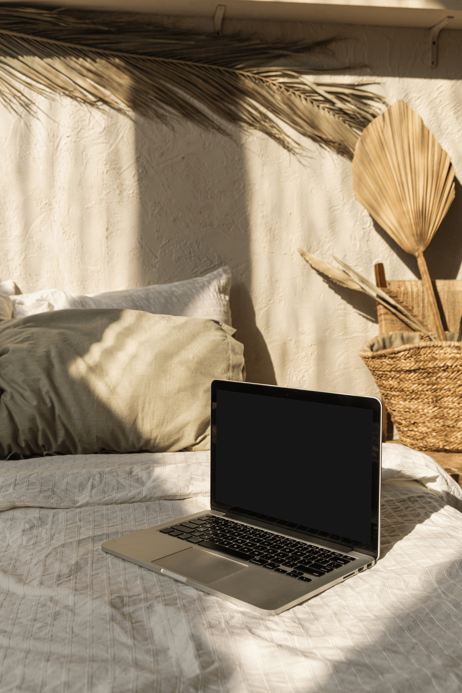 Laptop for online therapy for high-achieving womensitting on a bed with beige boho decorations in the background