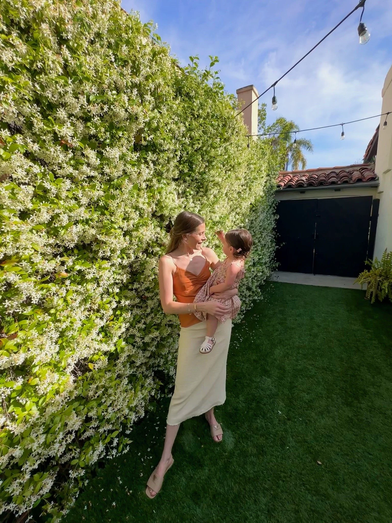 Rachel neporent - perinatel therapist in Los Angeles holding her daughter standing in front of a blooming hedge