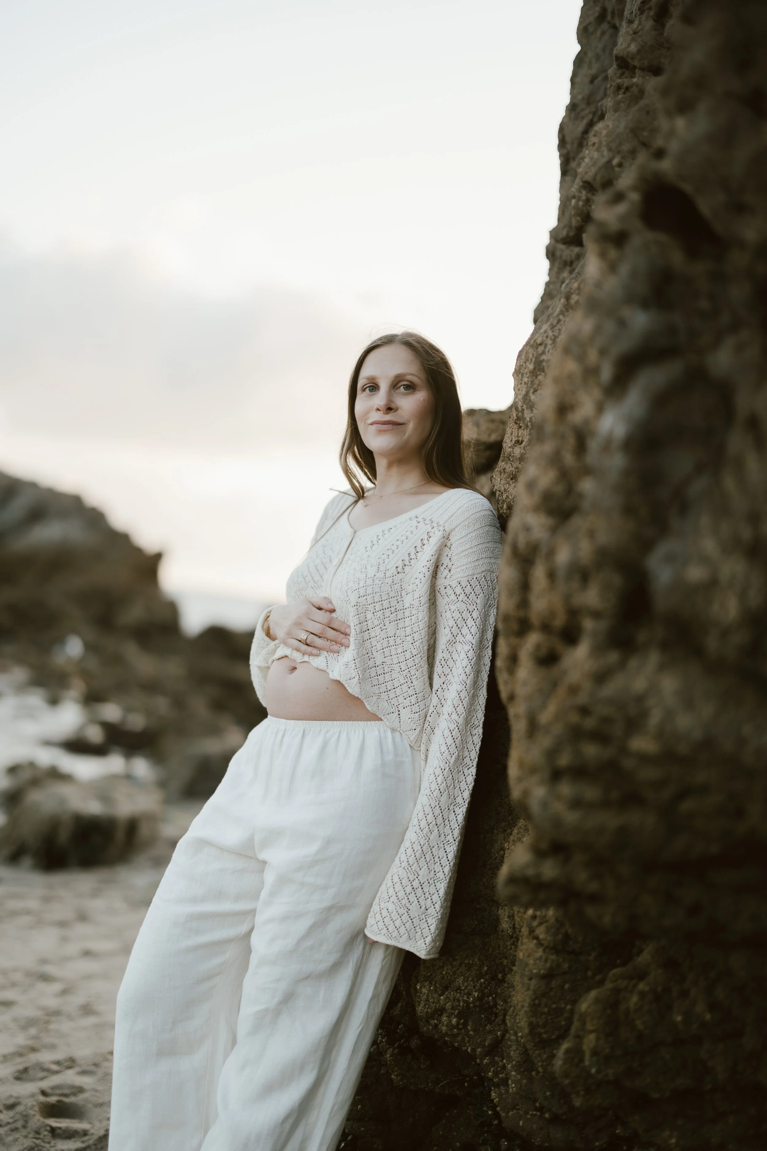 Perinatal therapist Rachel Neporent while pregnant standing in front of a rock on the beach in California