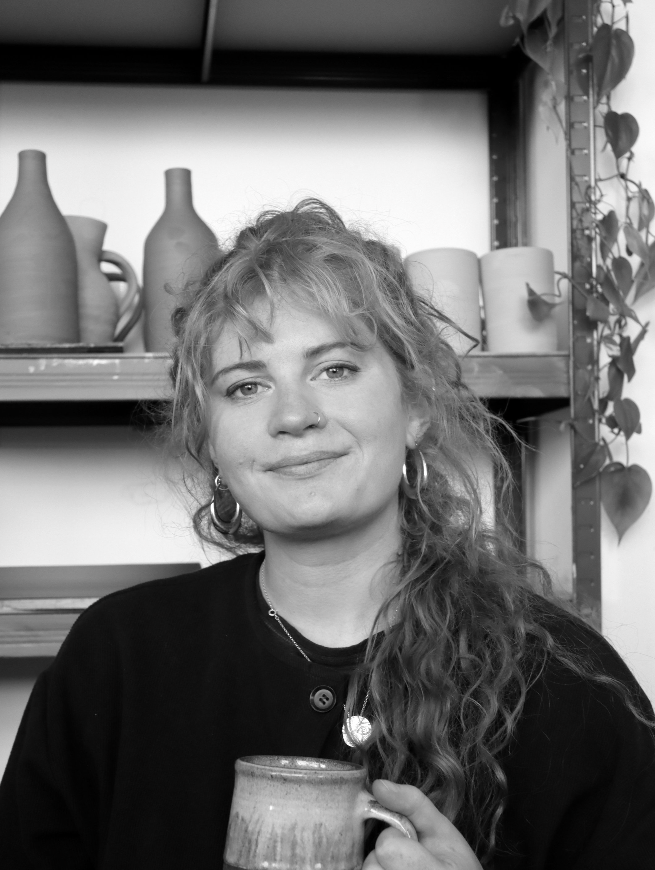 Person smiling at camera with pottery behind on shelves