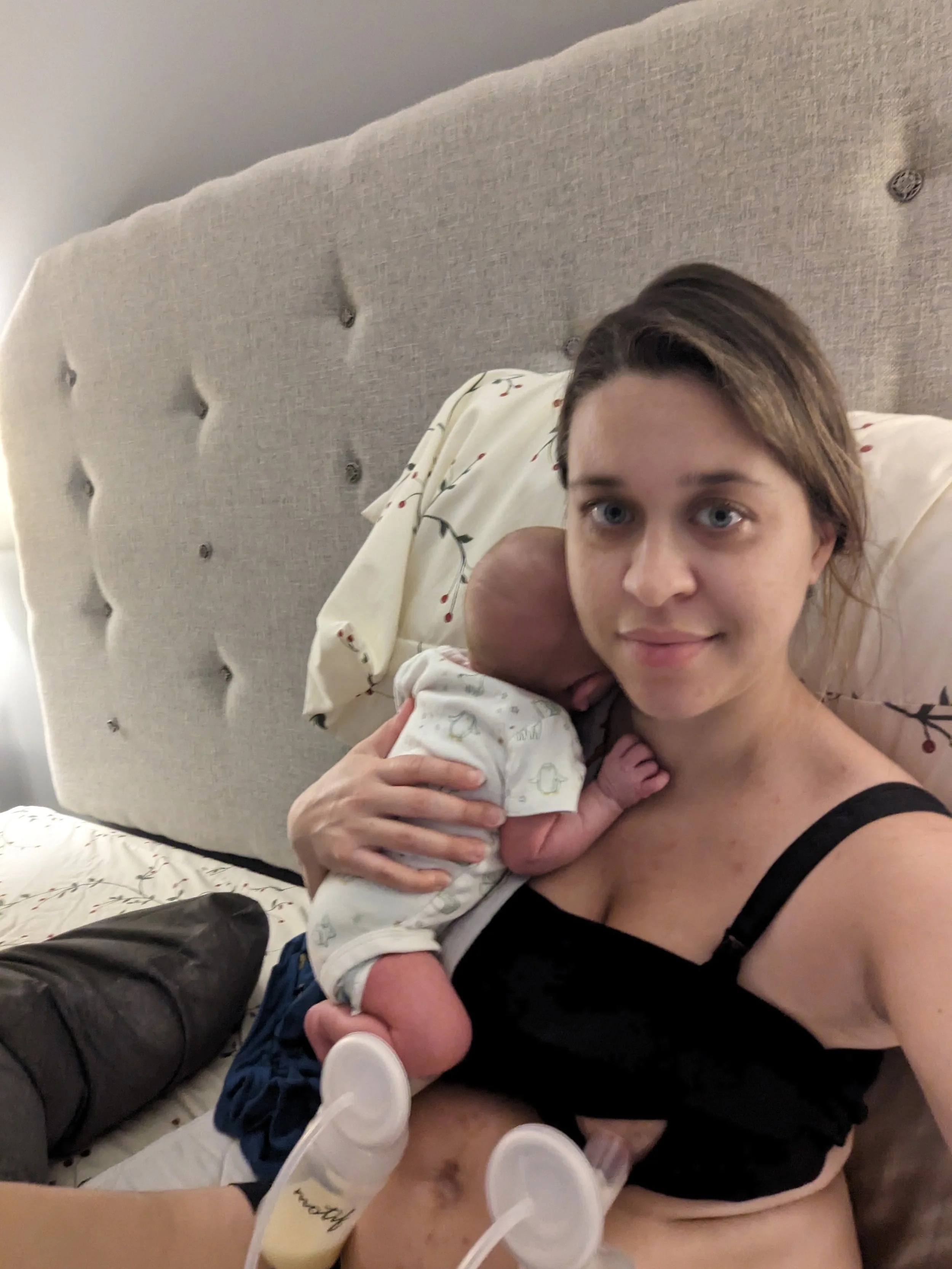 Fresh postpartum mom holding newborn while pumping breastmilk