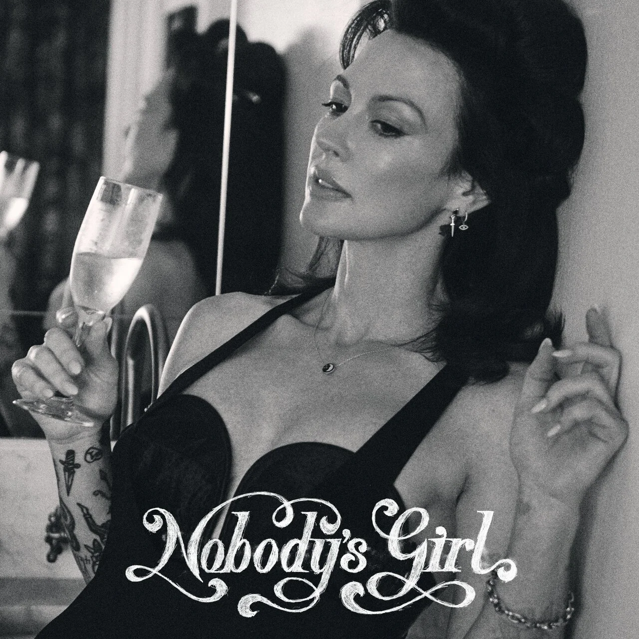 Amanda Shires leaning back with a class of Prosecco in her hand wearing a dress and looking contemplative.