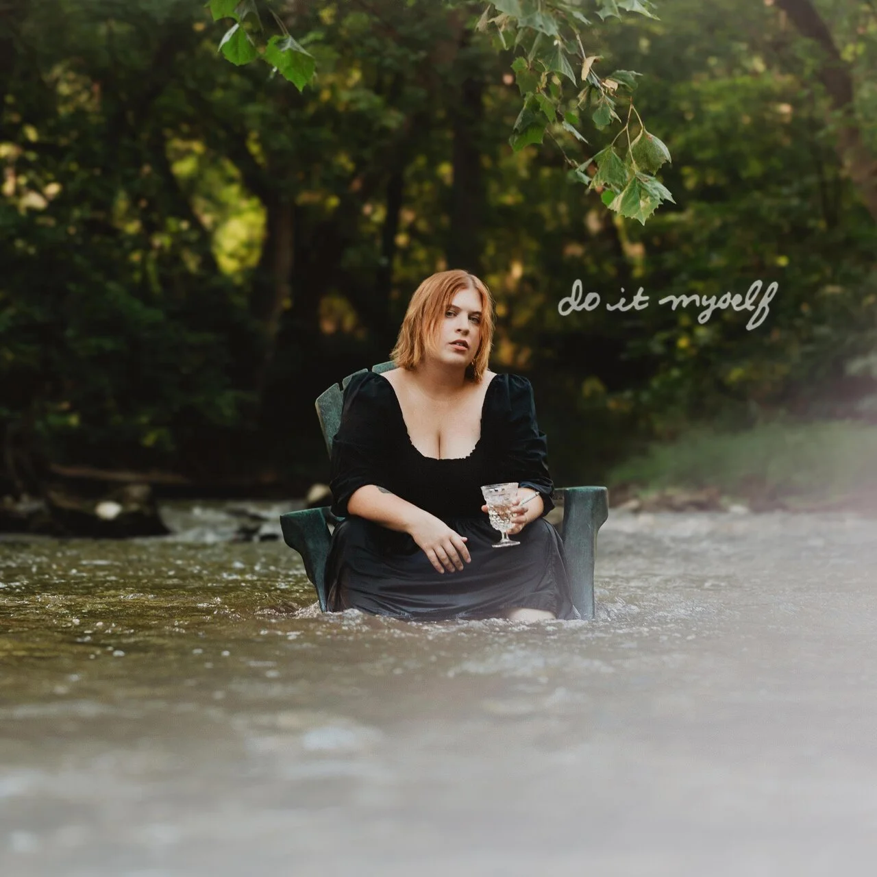 Photo of Olivia Ellen Lloyd sitting in an arm chair in a river holiding a wine glass.