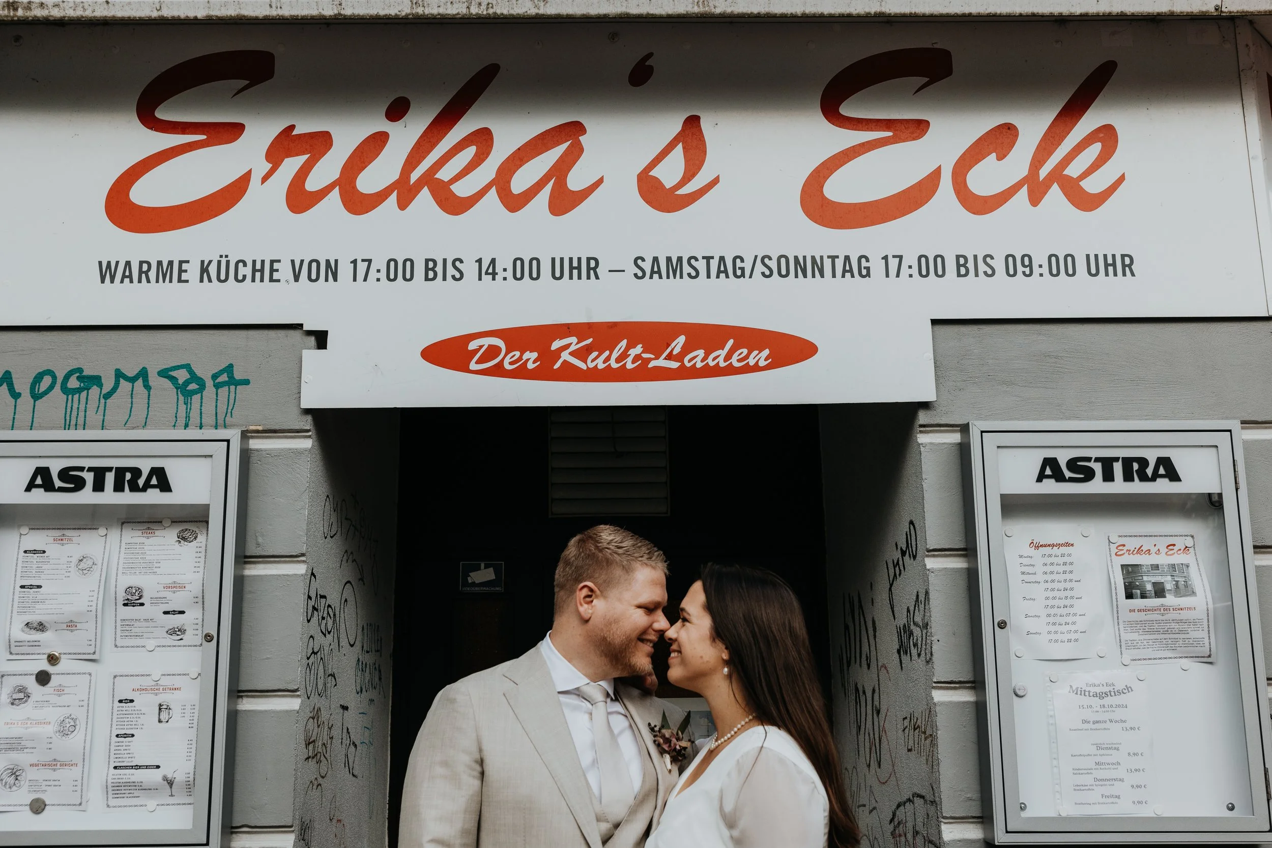 Glückliches Brautpaar steht vor dem Kult-Laden Erikas Eck und schaut sich verliebt an.