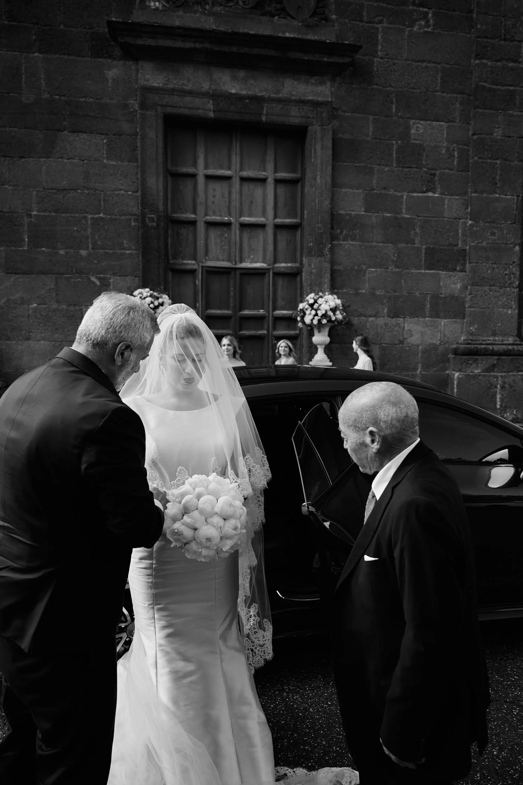 Bride exits the car and heads to the church doorway — black and white.