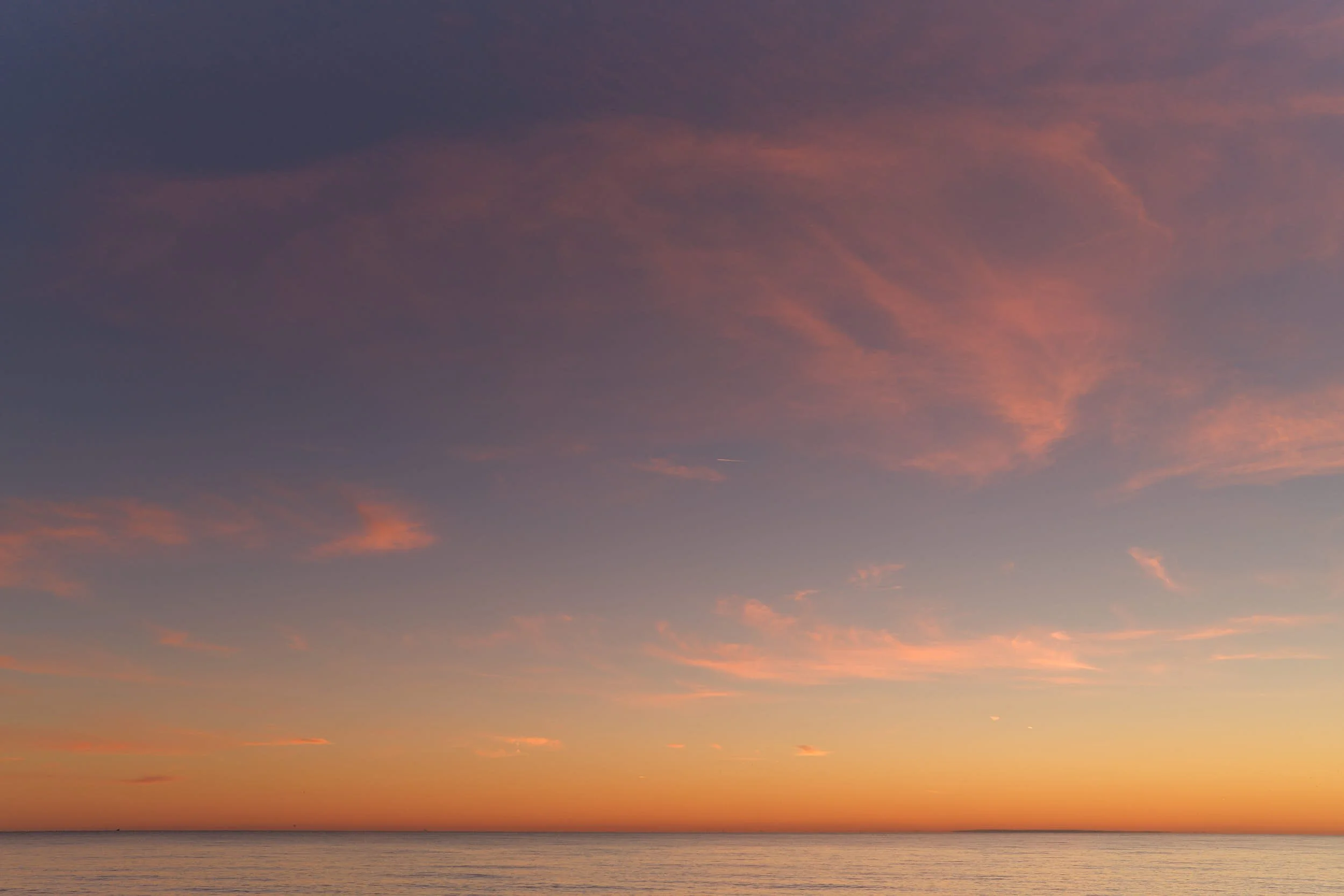 Pastel sunset over a calm sea, large expanse of sky with pink clouds fading into blue above a thin horizon line.