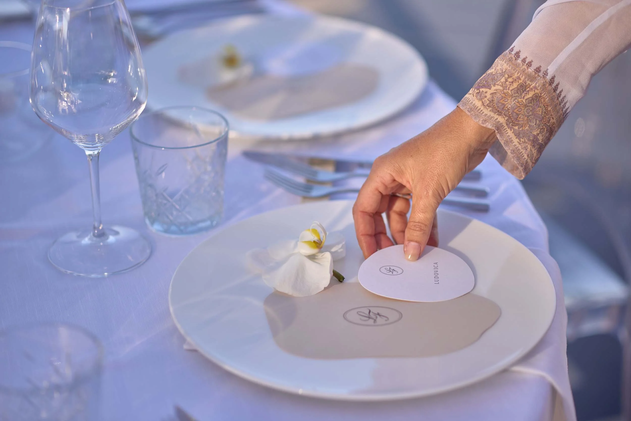 Minimal place setting with name card and orchid — refined wedding reception details, photographed in natural light.