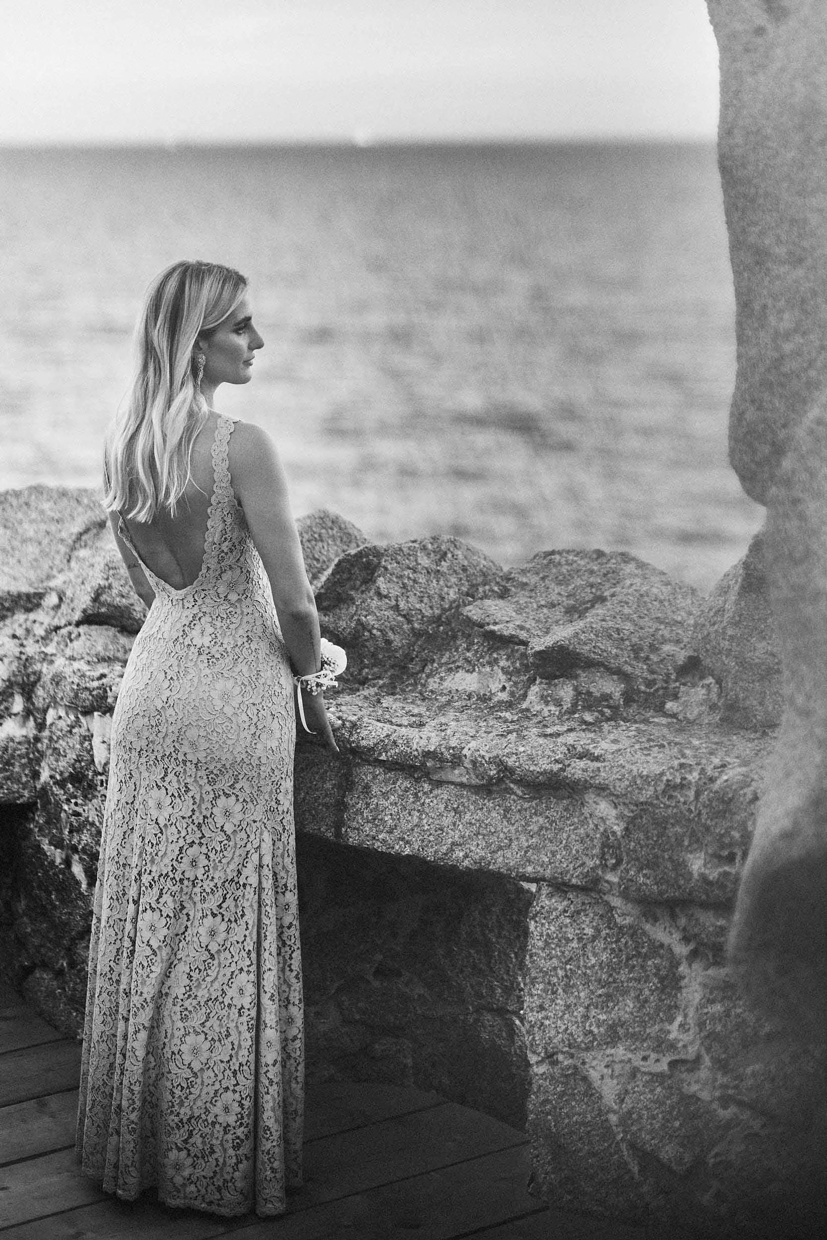 Portrait from behind of the bride’s sister, standing by a granite wall with the Sardinian coastline and sea in the background.