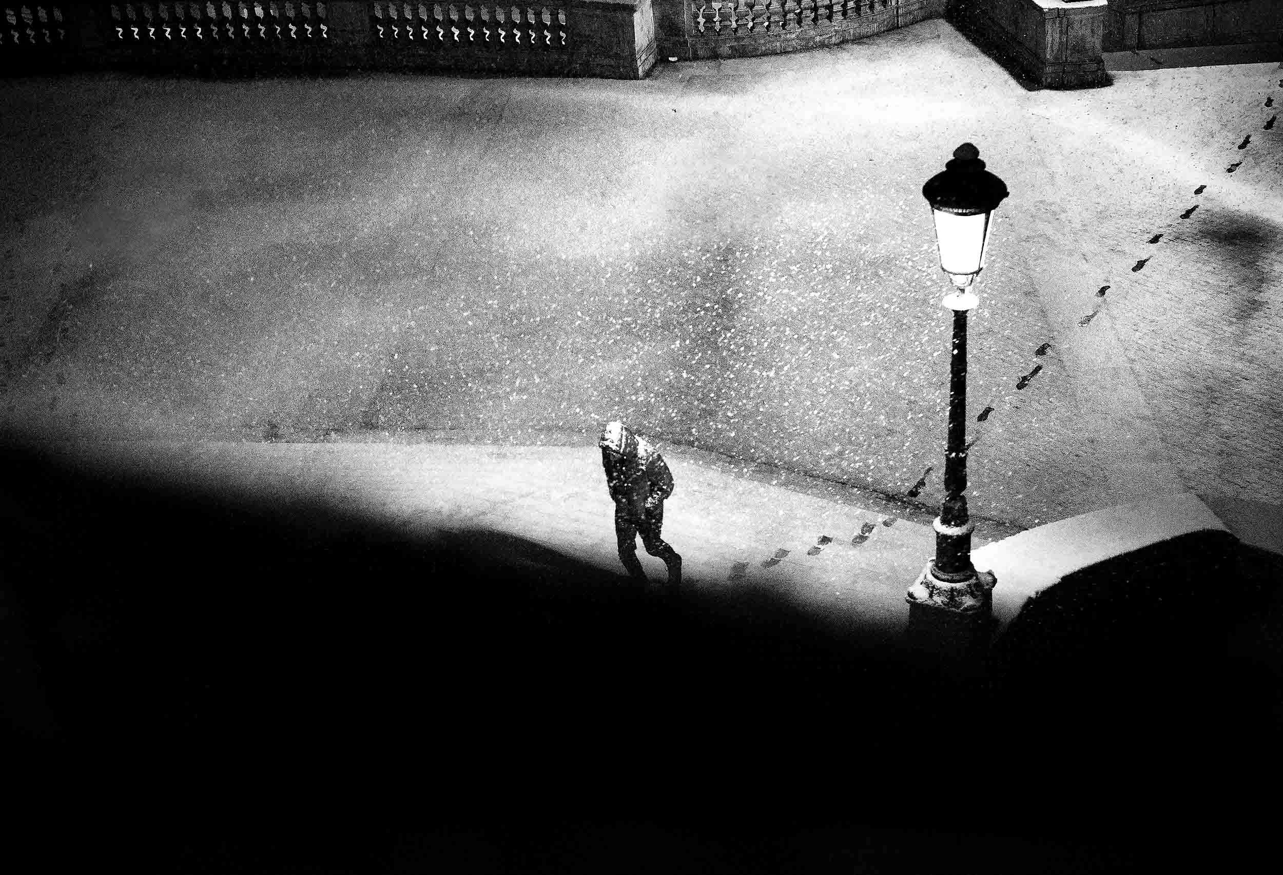 A man walking through snowfall in Piazza di Spagna, Rome, in a black-and-white photograph.